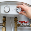 A hand adjusts the dial on a white electric water heater unit featuring green and red indicator lights.