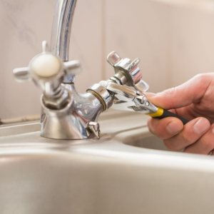 A person uses an adjustable wrench to loosen the metal nut on a silver kitchen faucet handle.