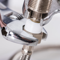An adjustable wrench tightening a metal pipe fitting with white threaded sealant.
