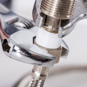 An adjustable wrench tightening a metal pipe fitting with white threaded sealant.