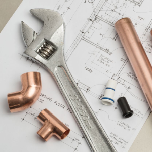A silver adjustable wrench, copper pipe fittings, and a copper pipe segment rest on a printed architectural floor plan.