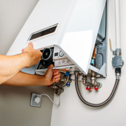 A technician adjusts the internal components of a white wall-mounted gas boiler.