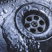 A stainless steel kitchen sink drain with water droplets and a thin layer of flowing water covering the surface.
