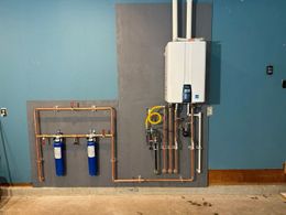 A wall-mounted tankless water heater and two water filtration units connected by copper piping on a blue wall.