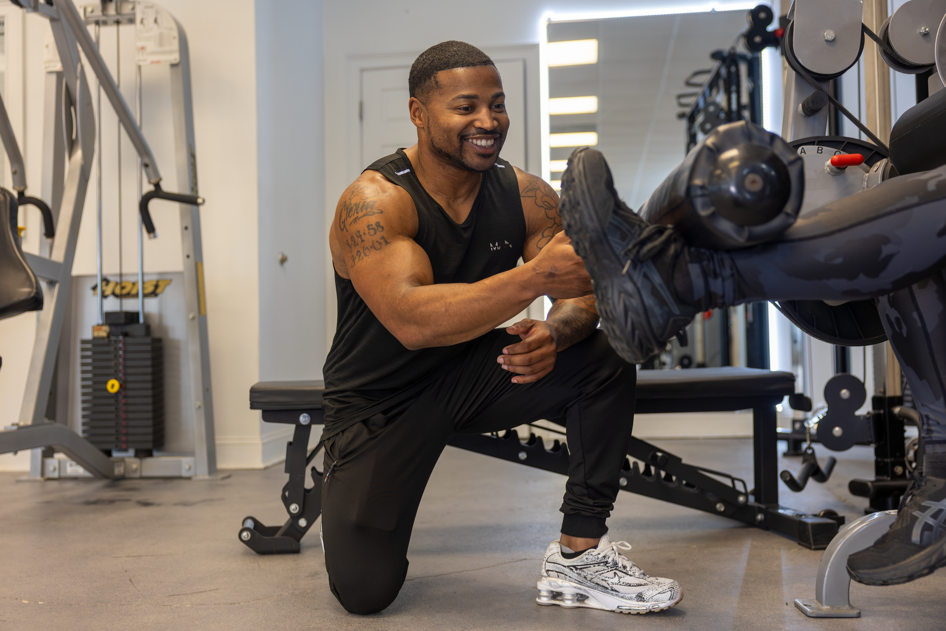 360 image fitness trainer Trey Johnson helping female client with leg extension exercises while wearing all black and smiling
