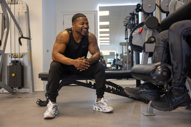 Trainer Trey Johnson owner of 360 Image Fitness smiling while coaching a female client on leg strengthening equipment