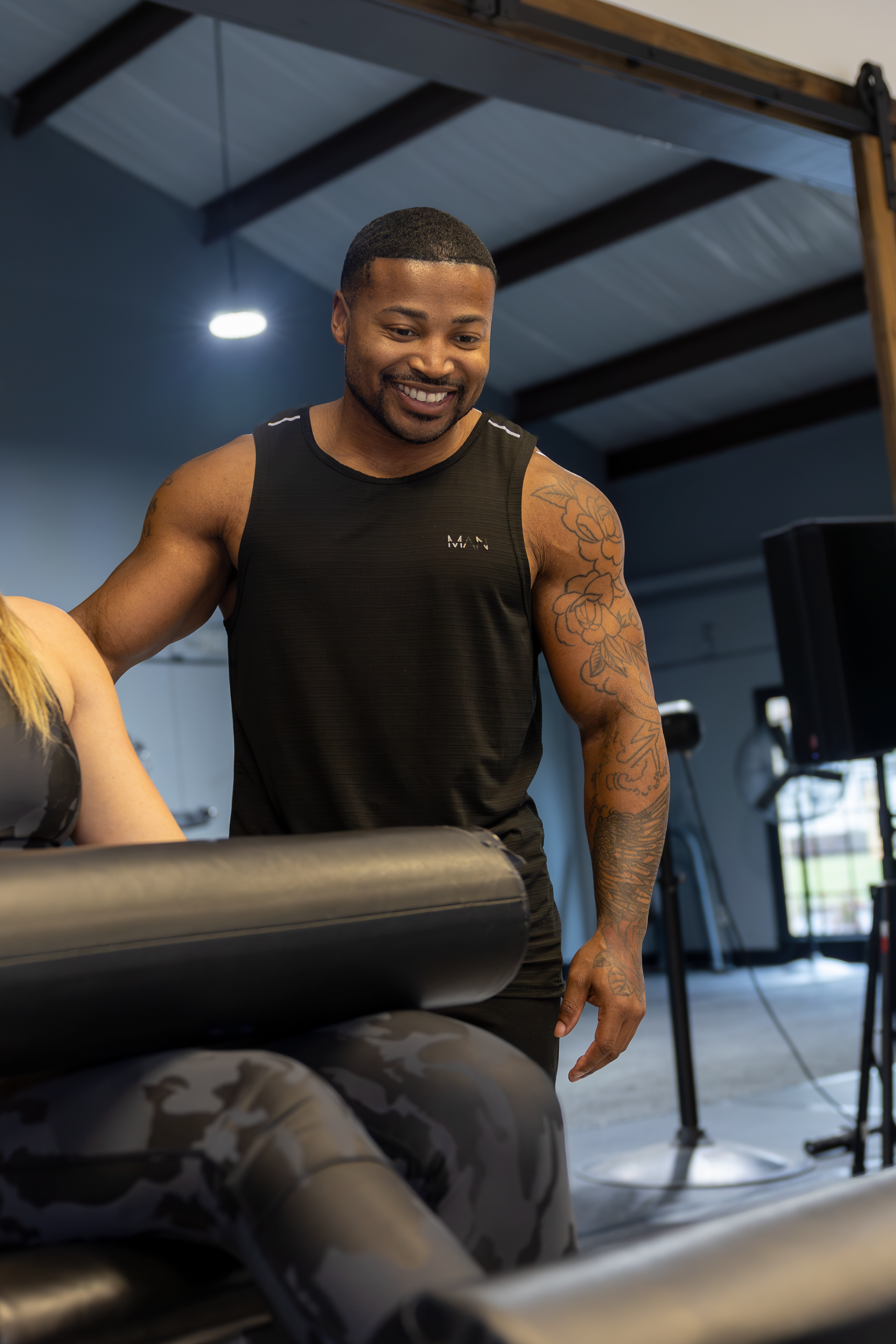 Trey Johnson from 360 Image Fitness in a black shirt smiling and helping a personal training client