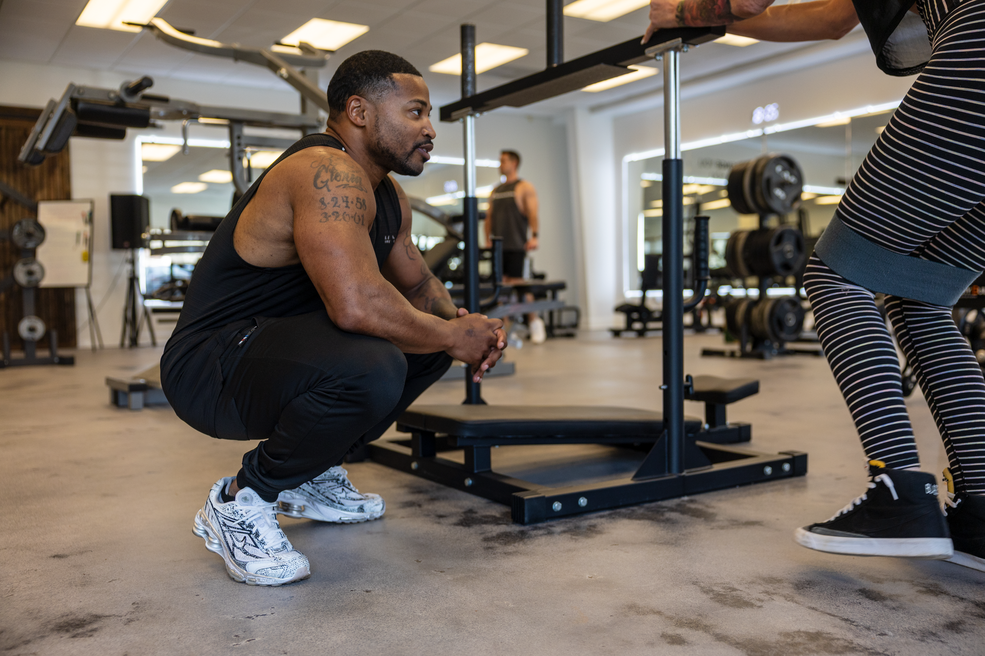 Trey Johnson training client during group fitness training session squatting down assisting client with correct fitness form