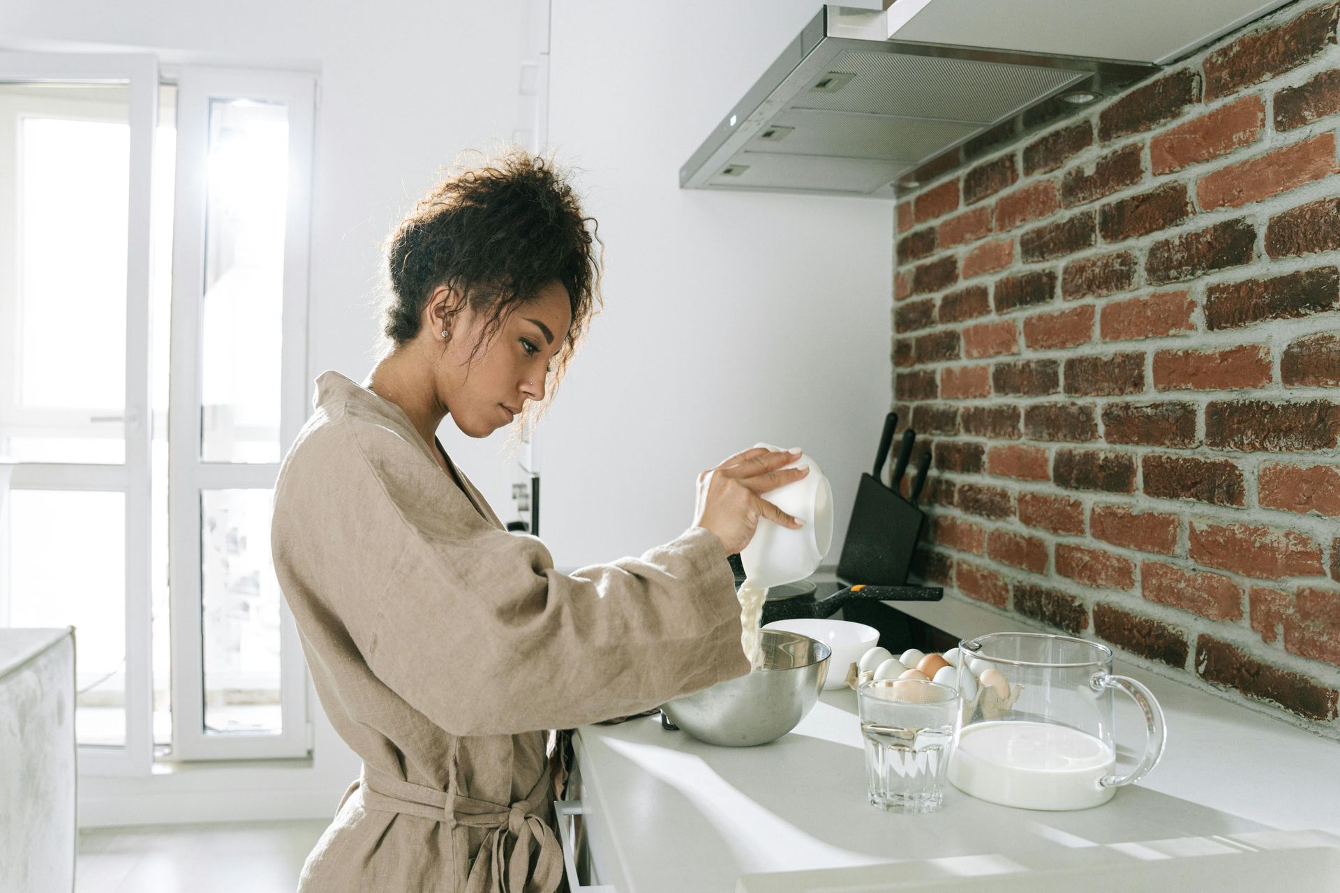 Person stirring a cup at a bright kitchen counter beside a brick wall
