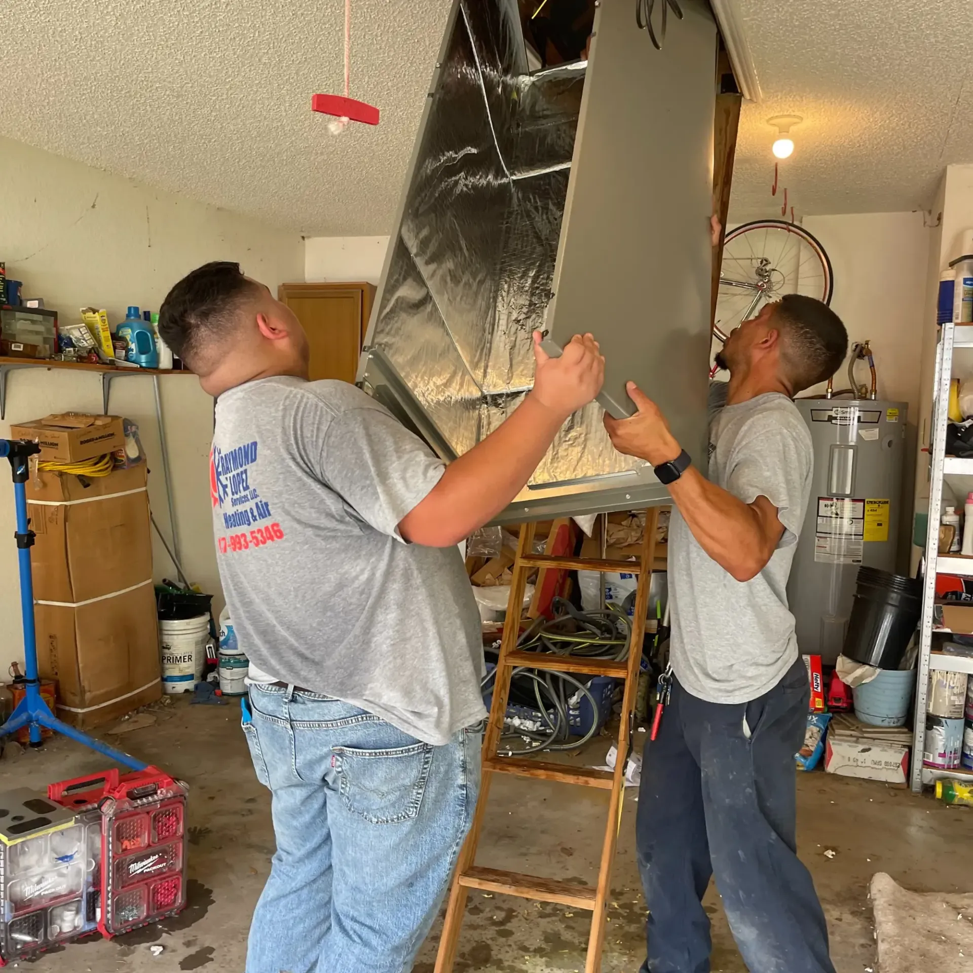Raymond Lopez Services, LLC. Heating & Air - Two men are carrying a large piece of metal in a garage.
