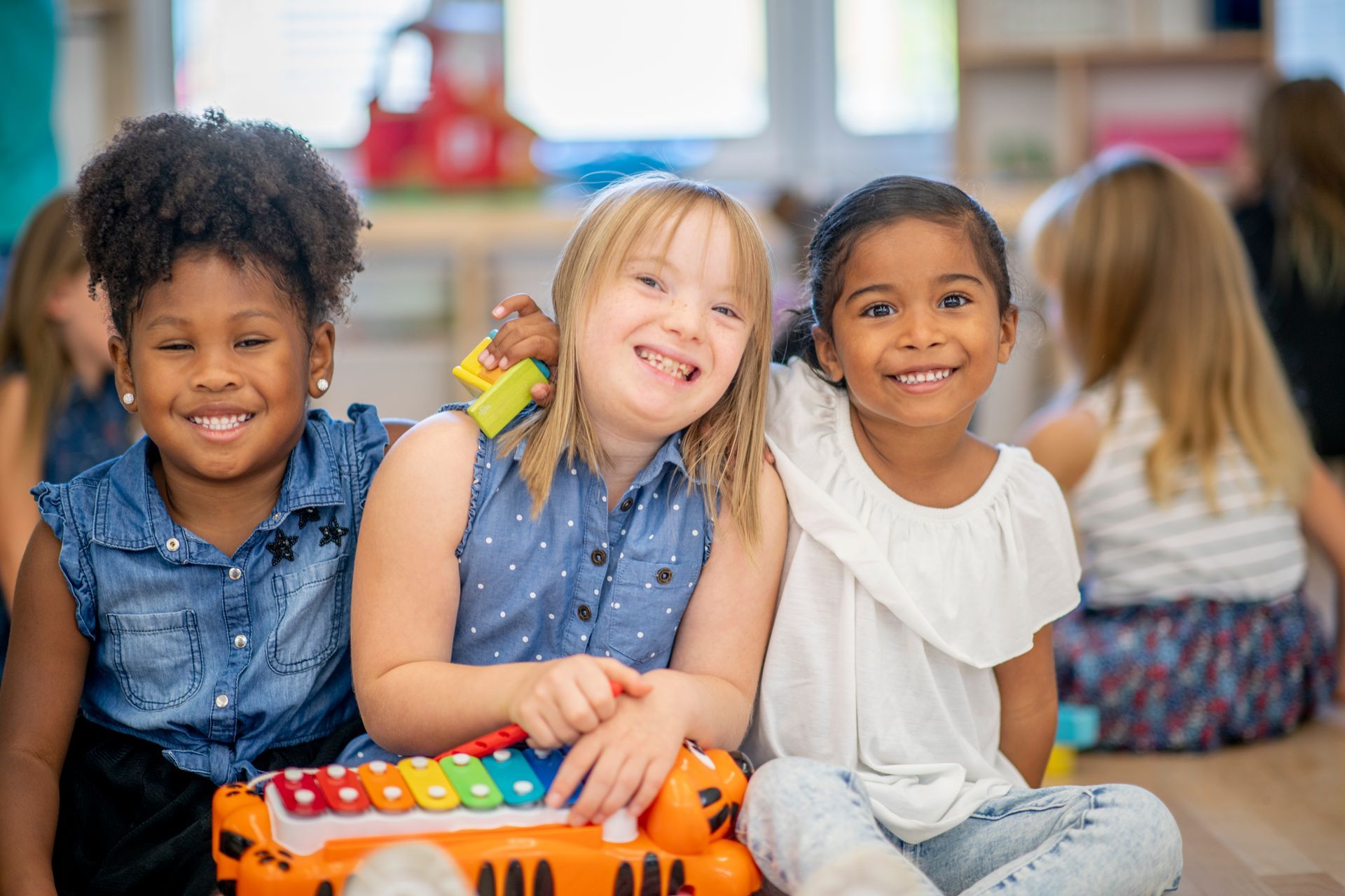 Three children smiling and playing with a colorful toy in a bright classroom