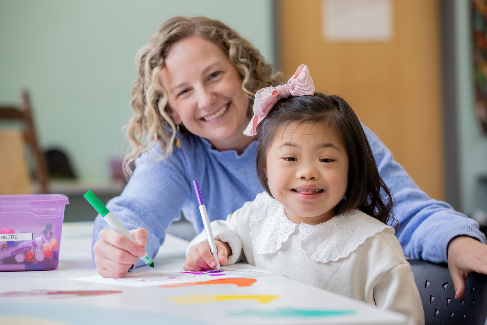 Teacher and child smiling while coloring at a table with markers and paper