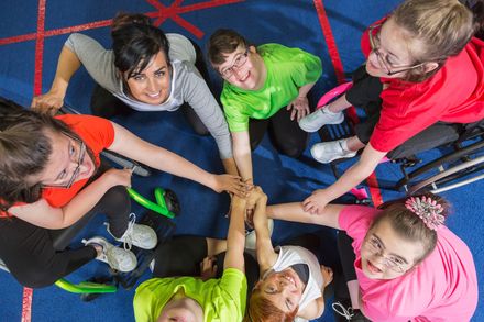 Children in colorful shirts stacking hands in a group circle on a blue floor