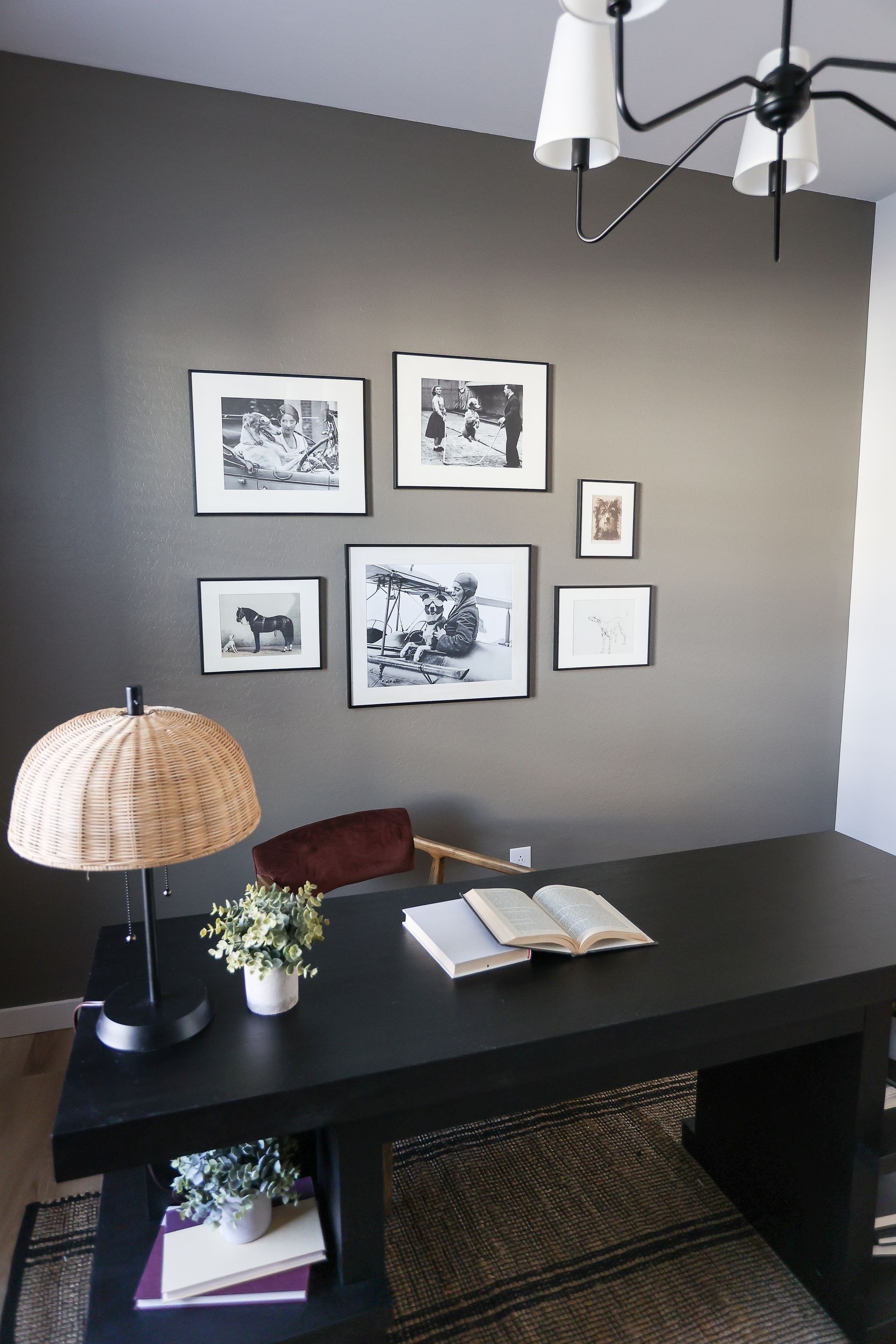 Home office desk with open notebook, small plant, framed wall art, and woven lamp in a gray room