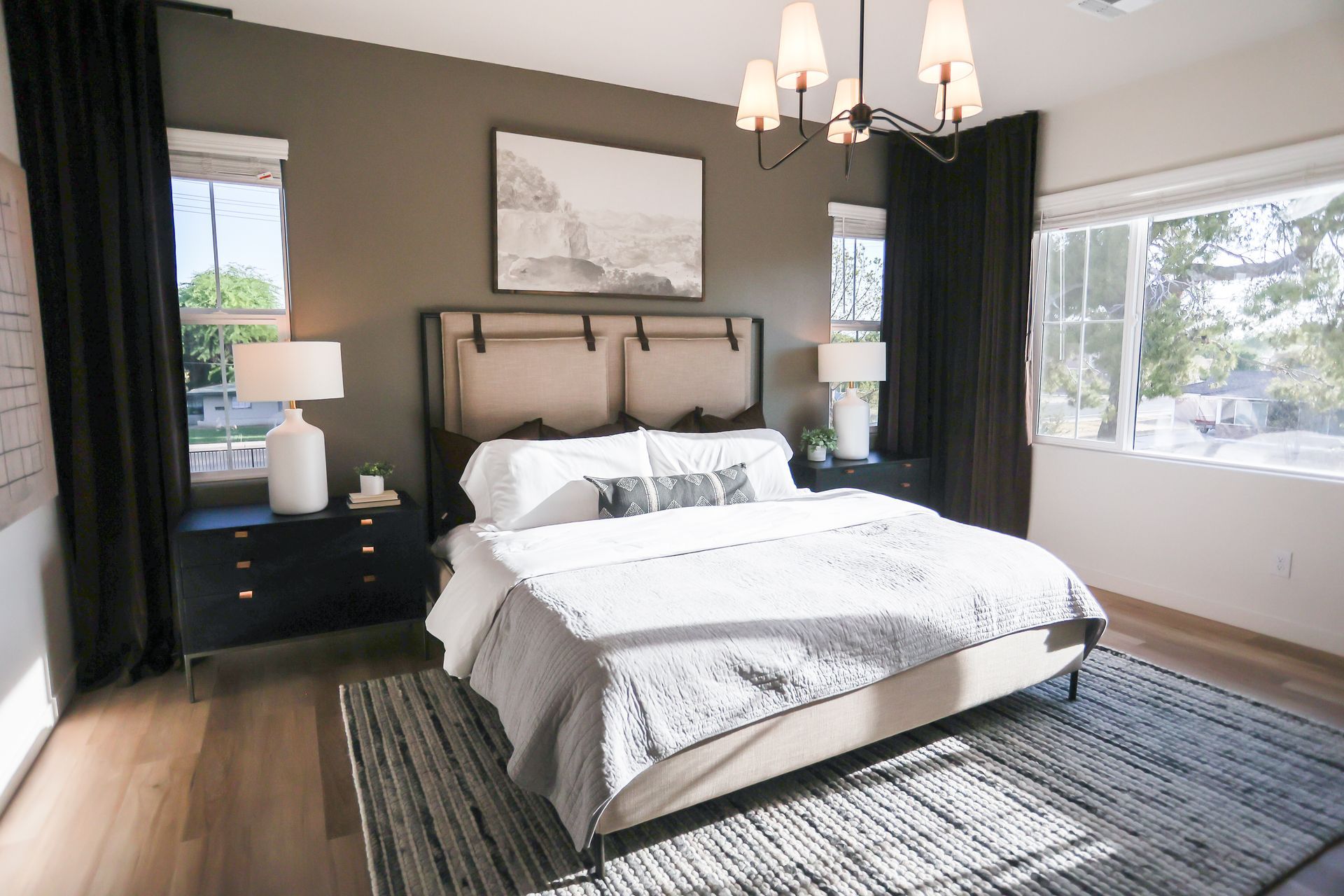 Bright bedroom with a bed, nightstands, chandelier, and large windows letting in natural light