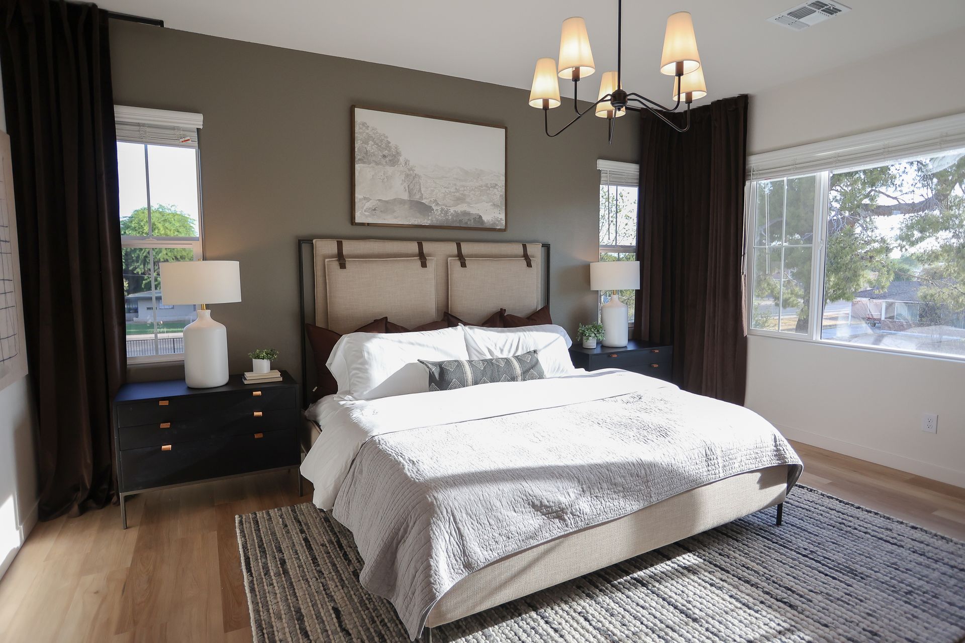 Bright bedroom with a large bed, dark curtains, chandelier, and natural light from windows