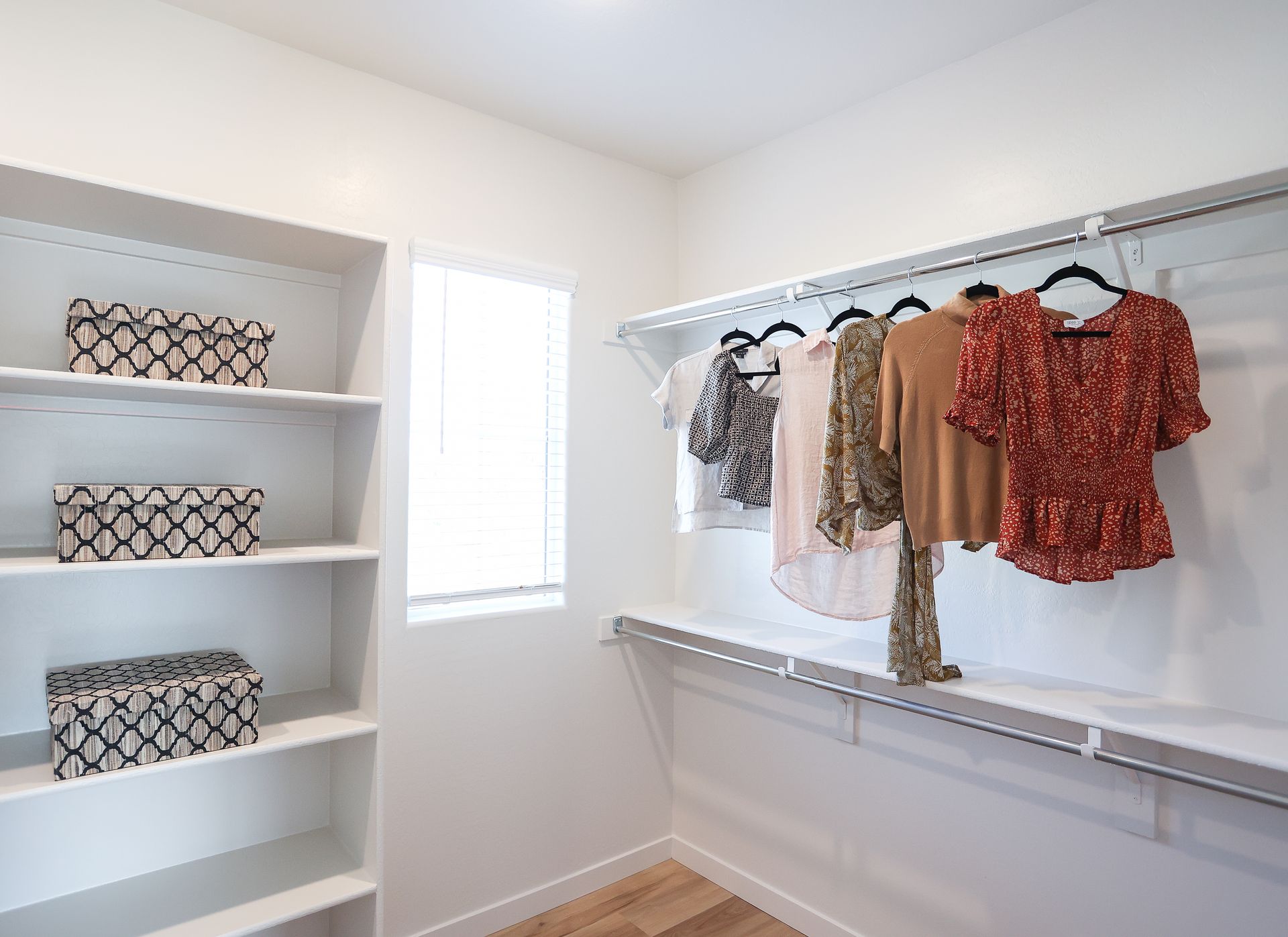 Walk-in closet with white shelves, hanging clothes, and patterned storage bins