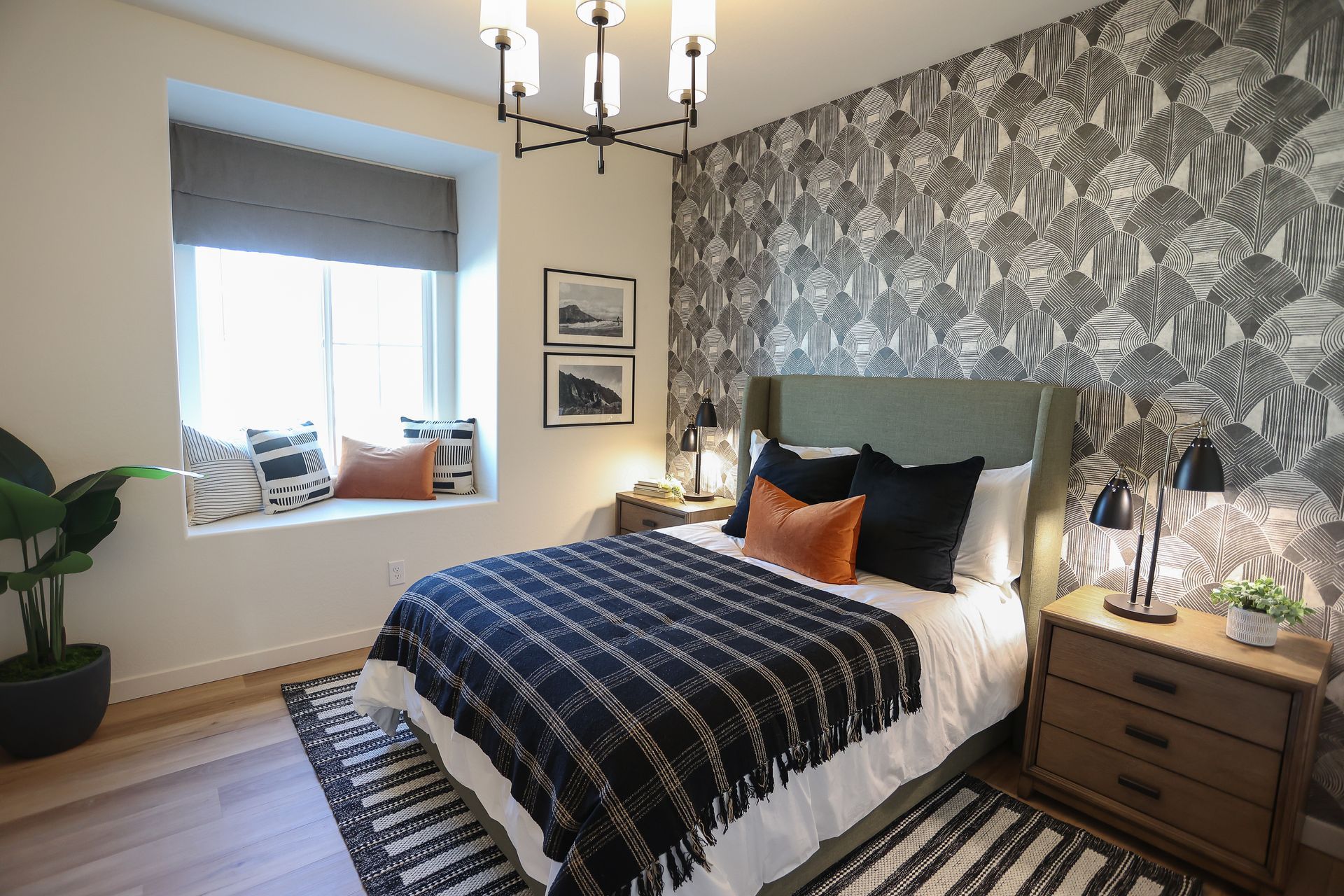 Cozy bedroom with patterned wallpaper, bed, nightstand, window seat, and soft gray-blue decor.