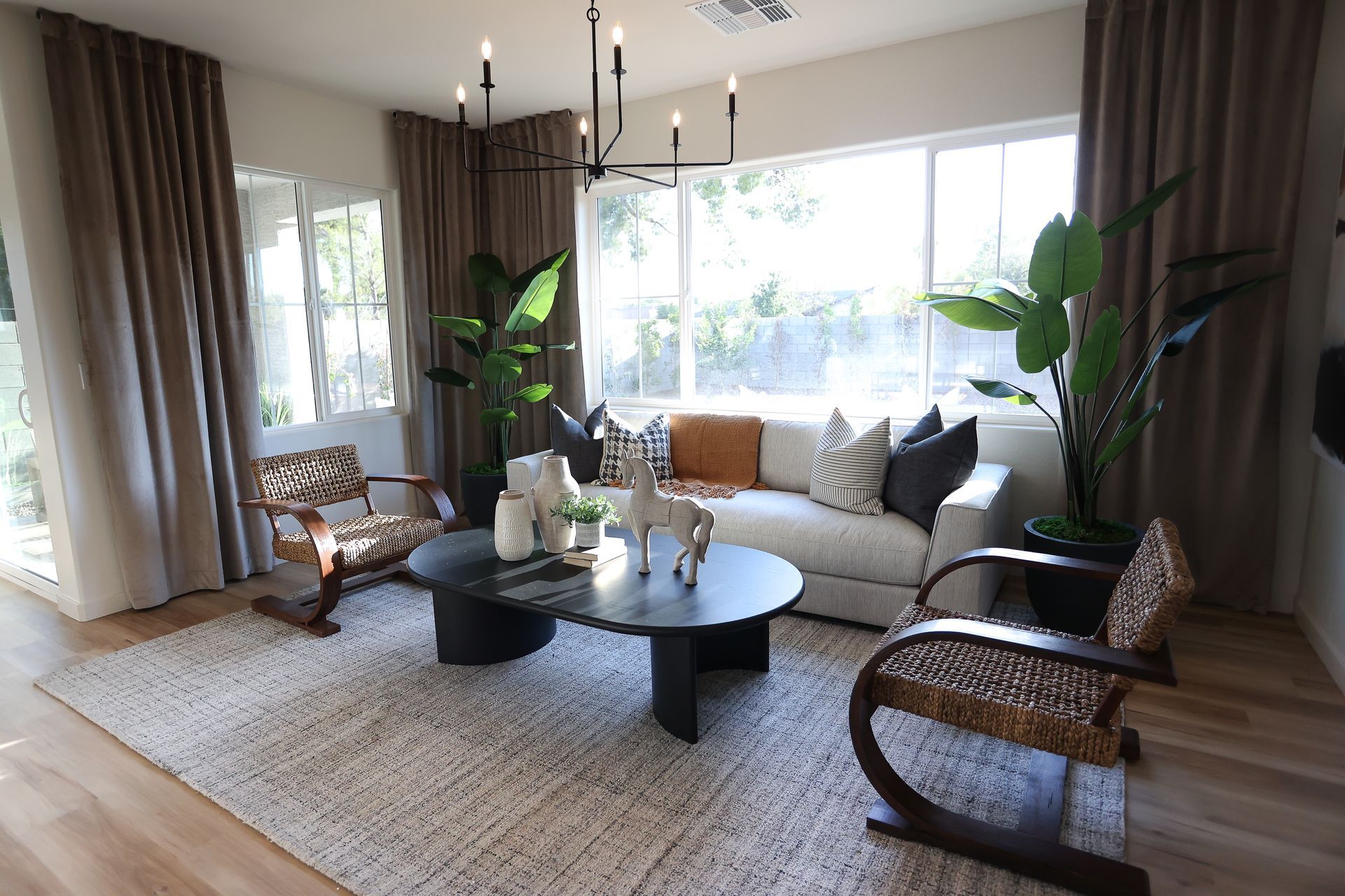 Bright living room with beige sofa, wicker chairs, coffee table, large windows, and potted plants