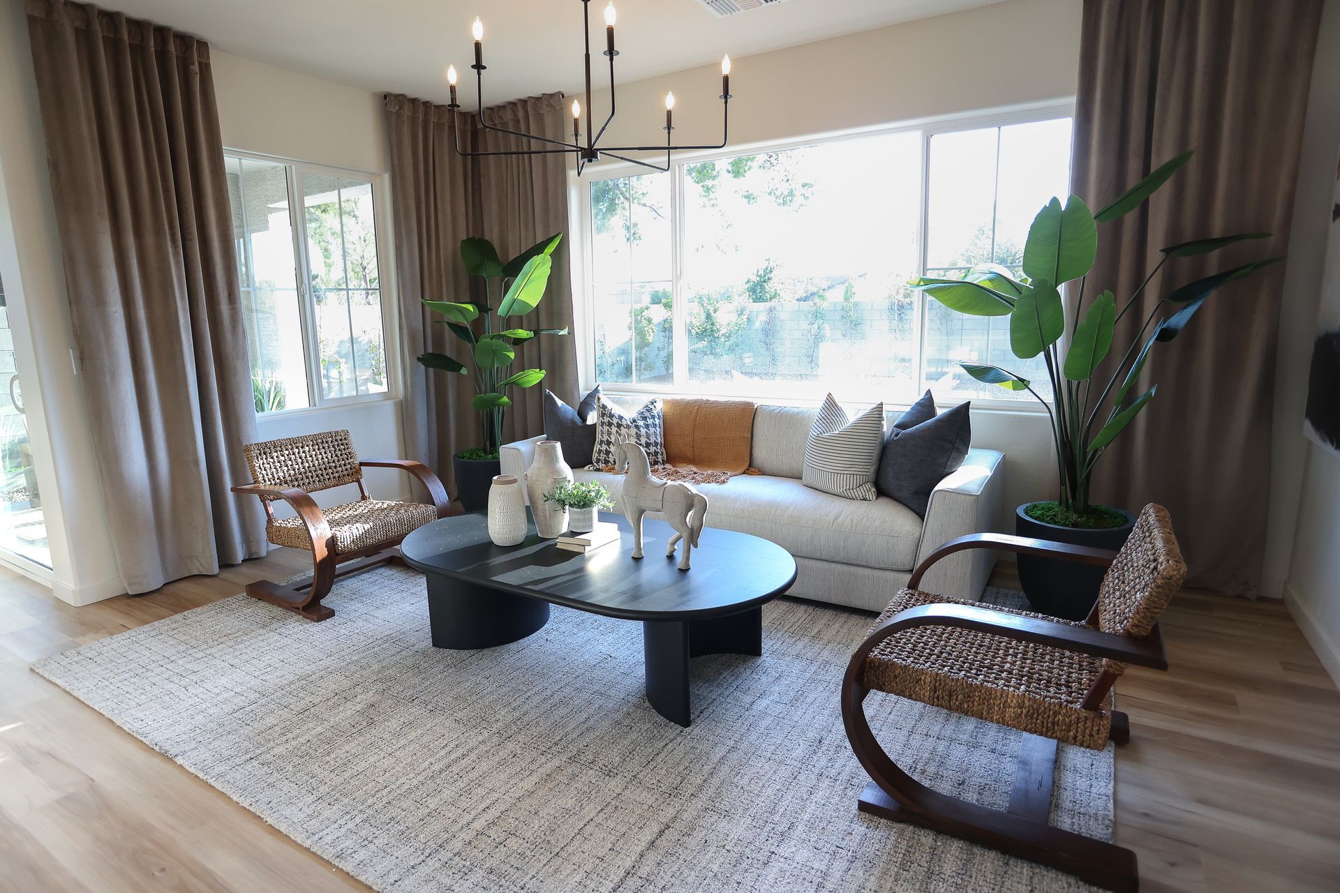 Bright living room with wicker chairs, sofa, coffee tables, large windows, and sheer curtains