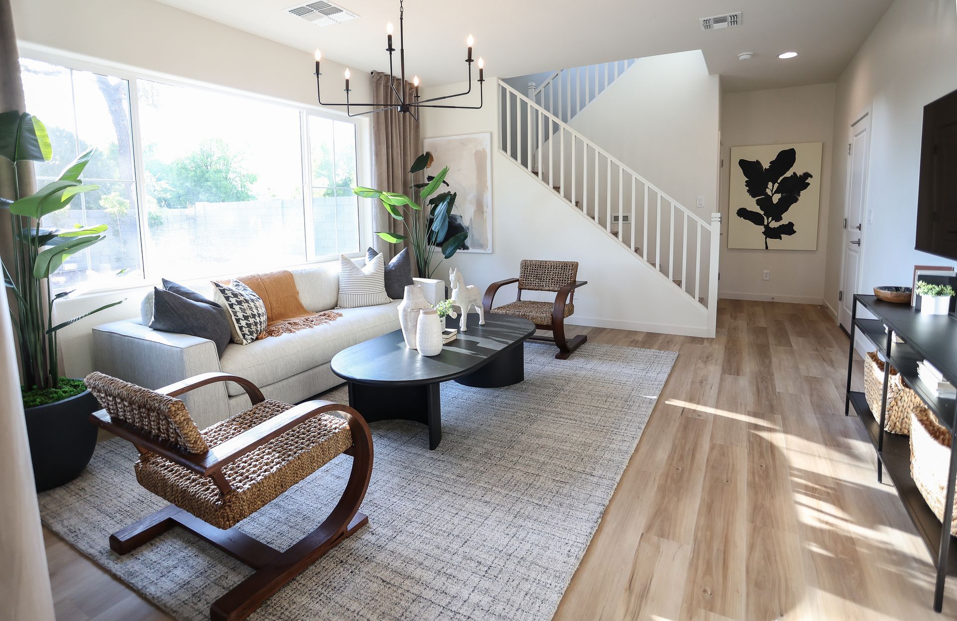 Bright living room with sofa, coffee table, staircase, large windows, and sunlit wood floor