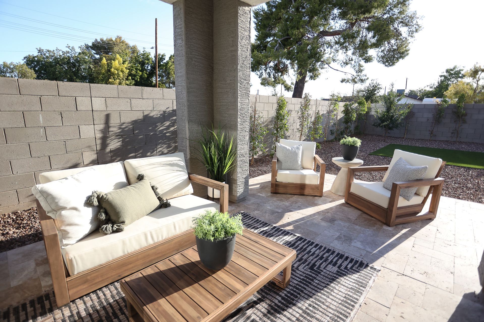 Sunny patio with white and wood lounge chairs, beige sofa, and potted plants under a covered pergola.
