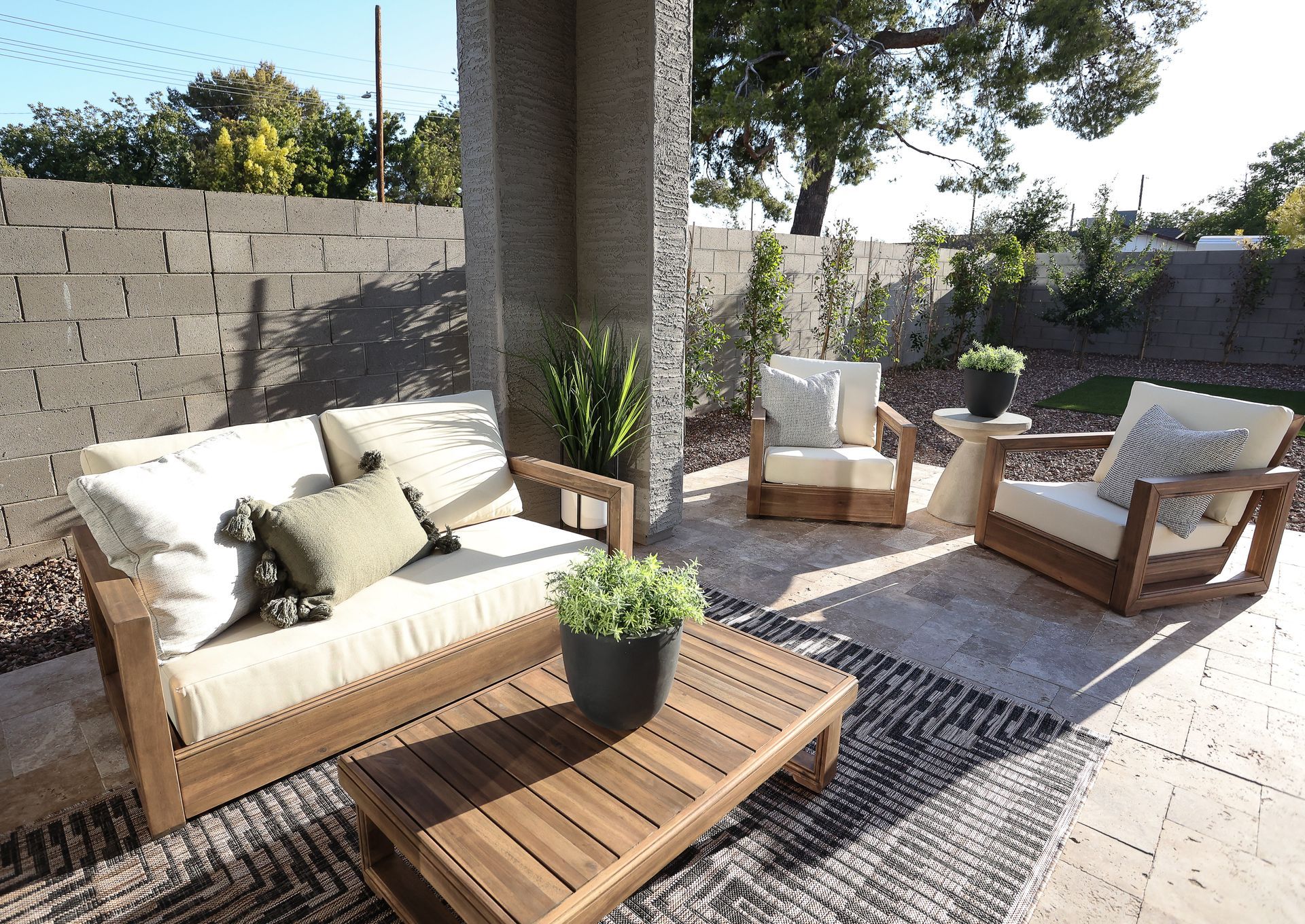 Sunlit patio with white outdoor sofas, wooden coffee table, and potted plants around a column