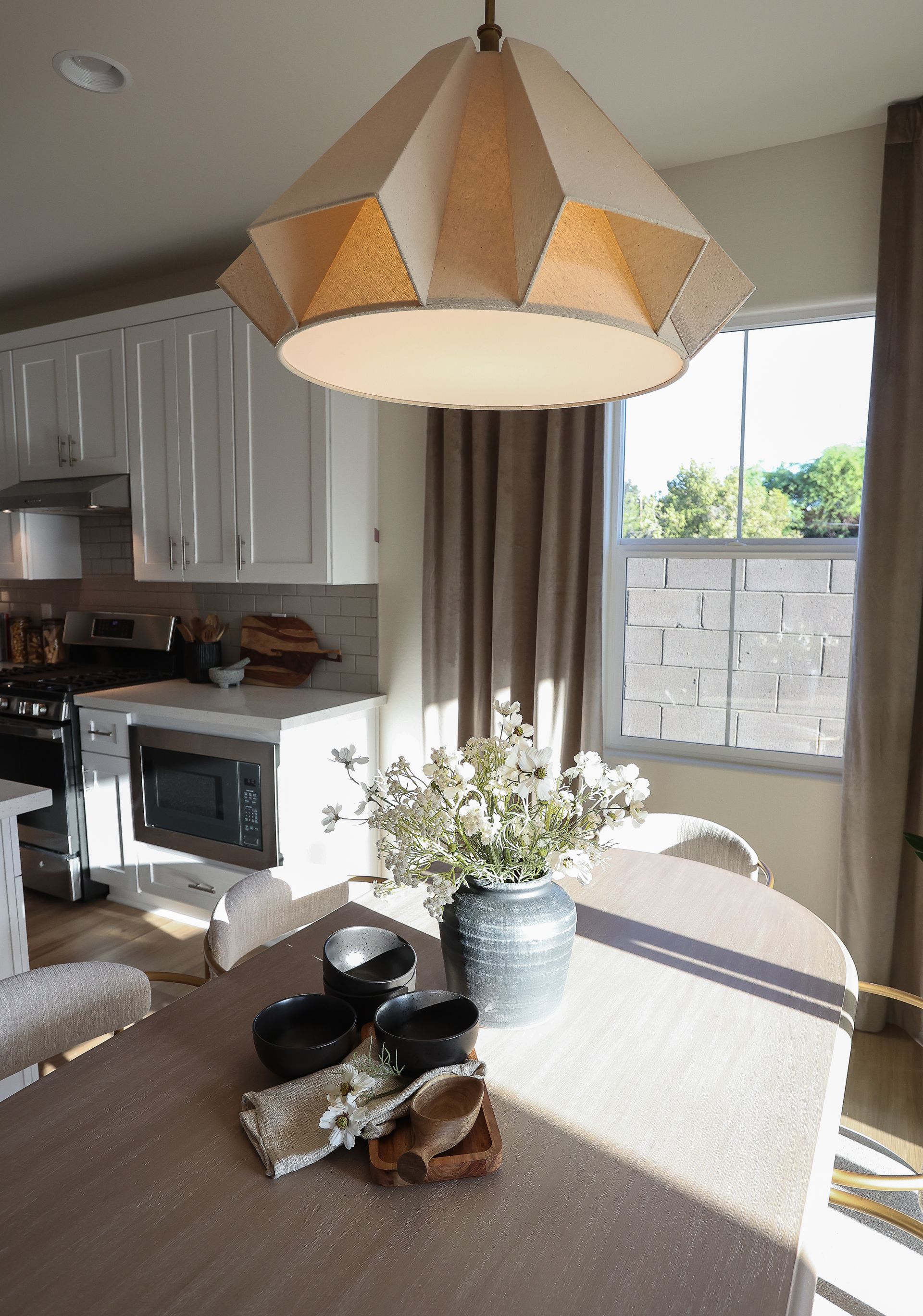 Bright dining table with flowers in a vase under a geometric pendant light in a sunlit kitchen.