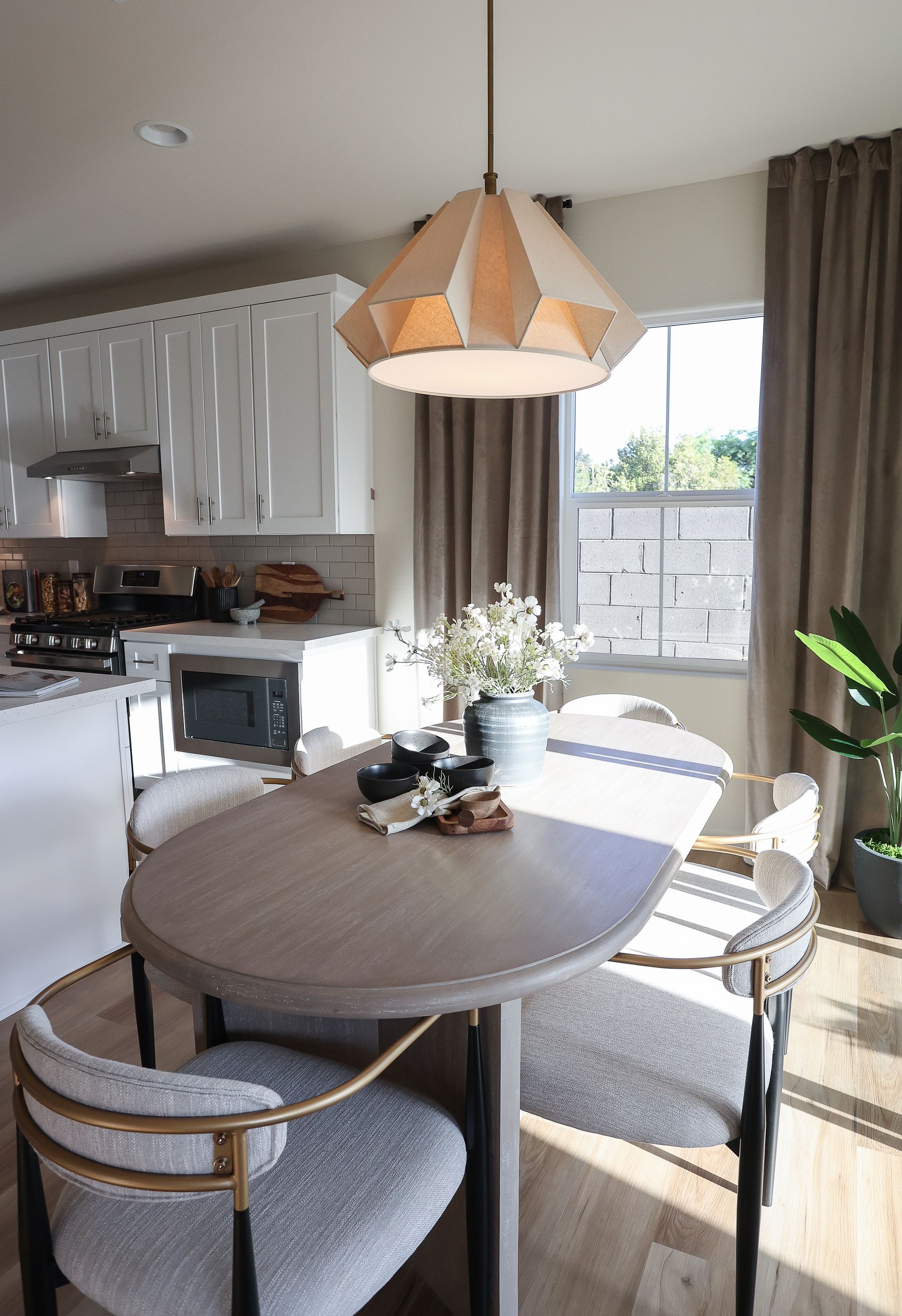 Bright dining area with oval table, cushioned chairs, pendant light, and large windows with curtains