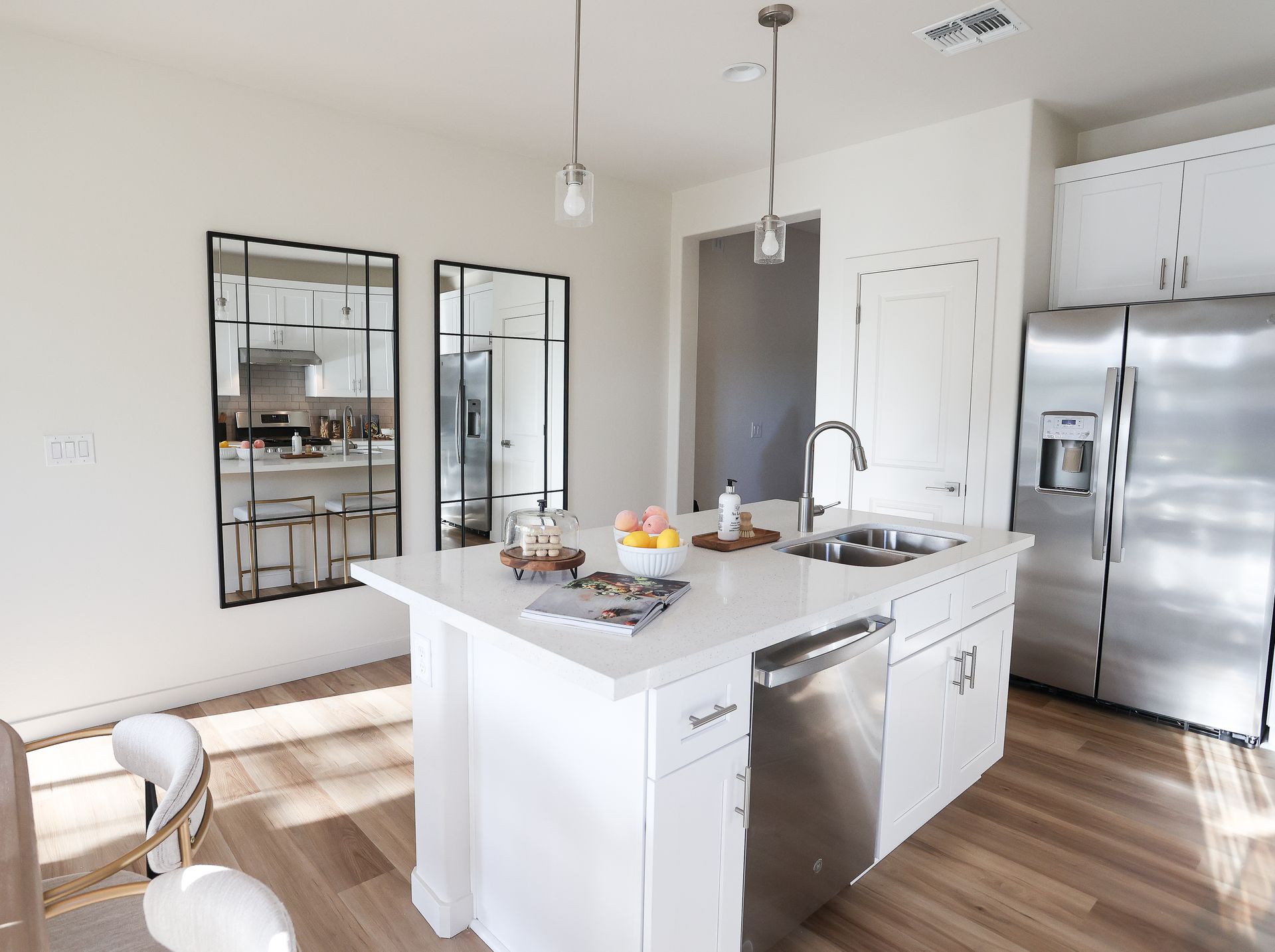 Modern white kitchen with island, stainless steel appliances, and black-framed mirrors on the wall