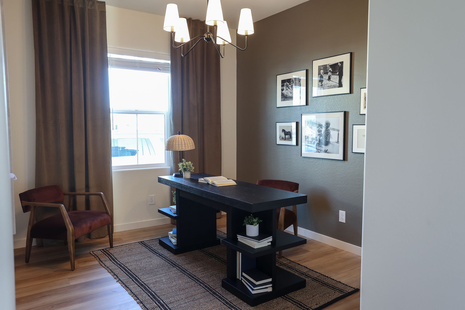 Home office with dark desk, window, brown curtains, framed wall art, and striped rug