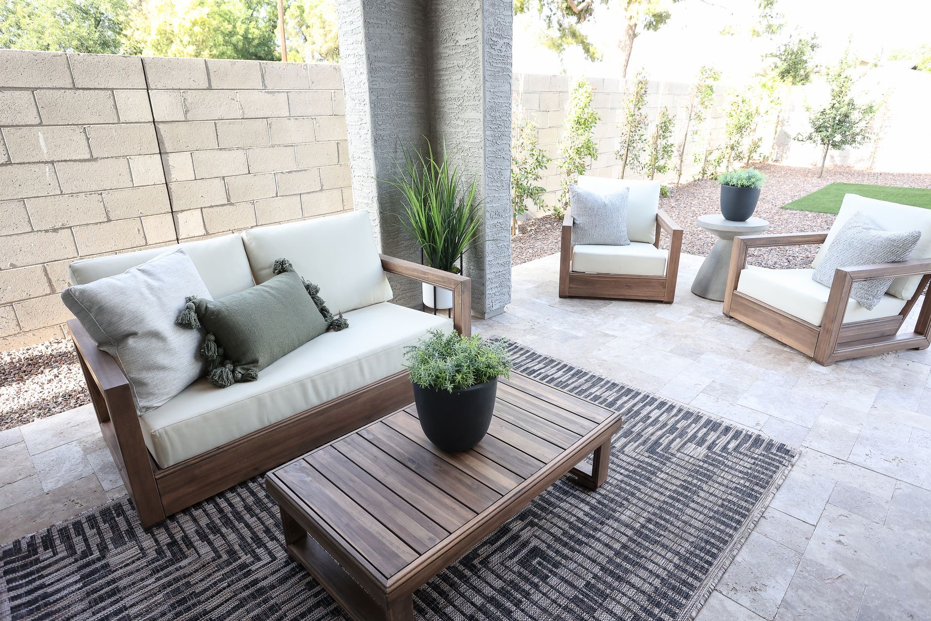 Outdoor patio seating area with wooden furniture, white cushions, and potted plants on a rug