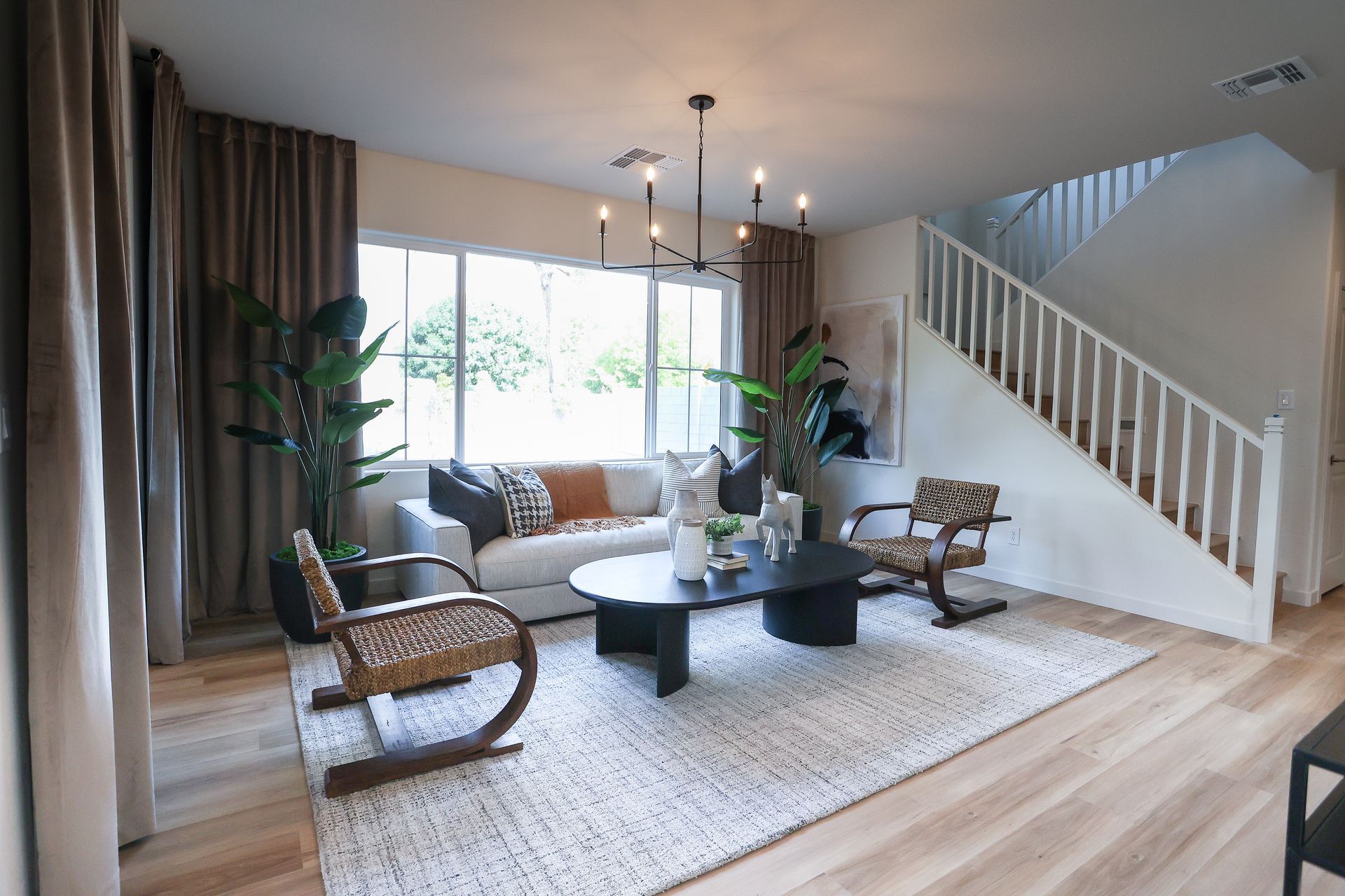 Bright living room with sofa, wicker chairs, coffee table, rug, and staircase by large windows
