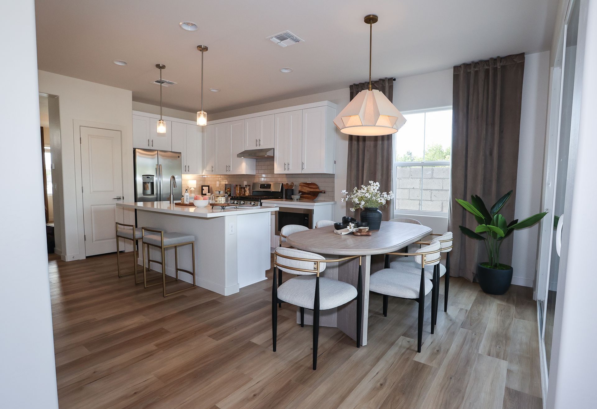 Bright modern kitchen and dining area with white cabinets, island, wood floors, and a round table by a window.