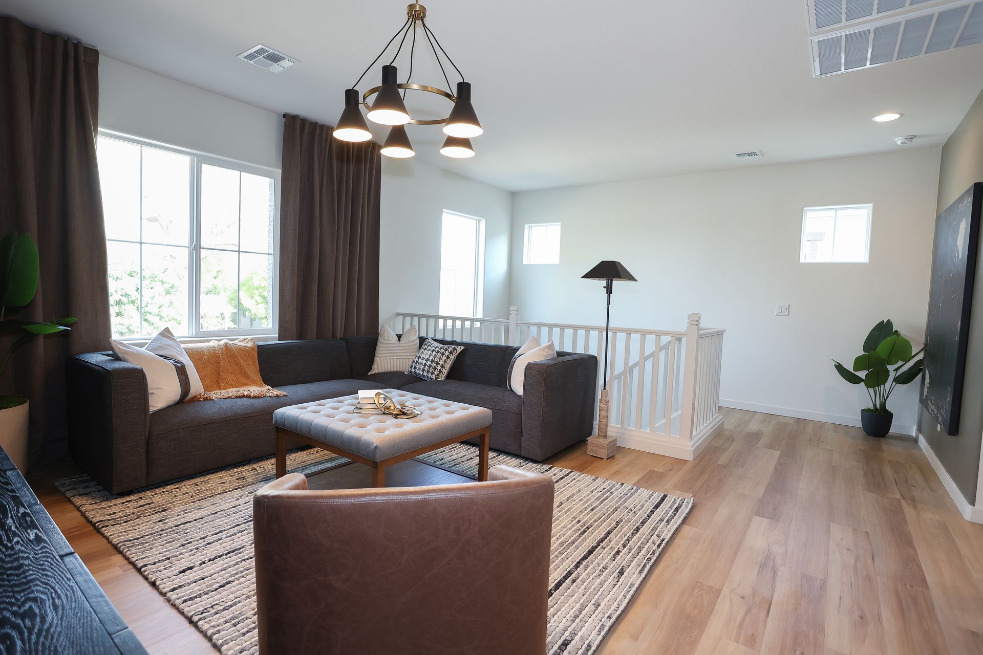 Bright living room with gray sectional, brown chairs, rug, wood floor, and large windows