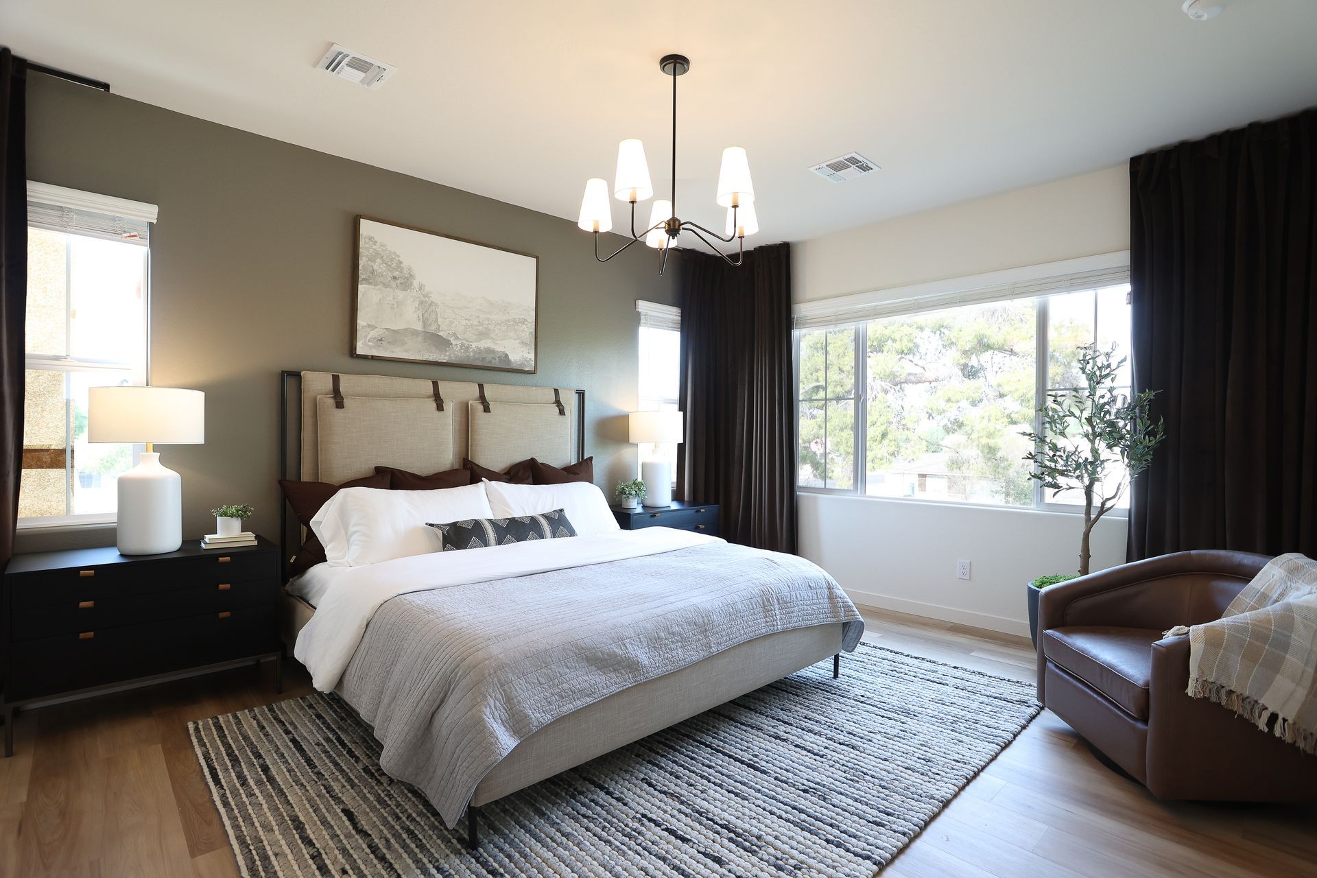 Bright bedroom with a large bed, chandelier, dark curtains, and a seating area by the window.