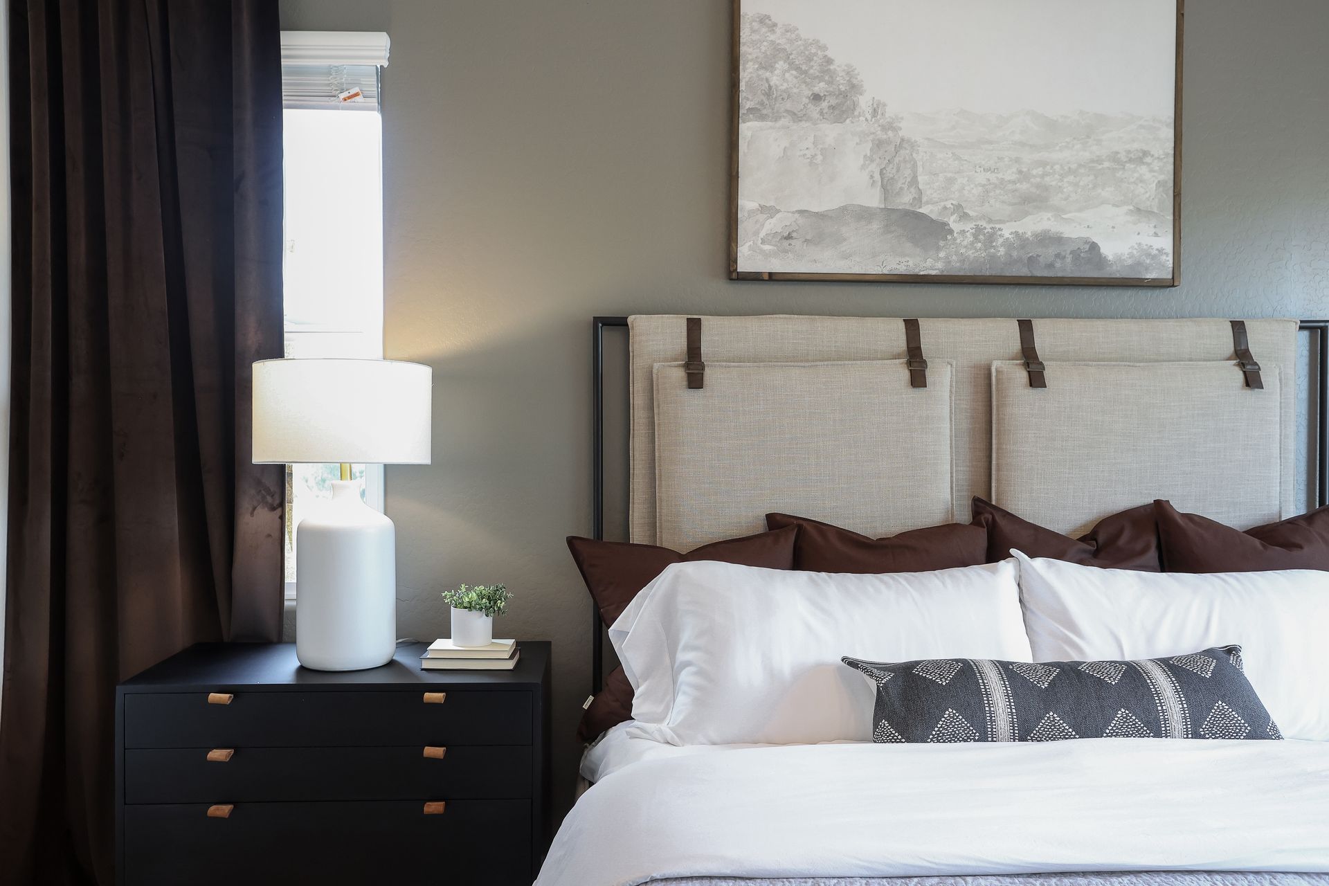Bedroom with a white bed, dark nightstand, lamp, and framed artwork above the headboard.
