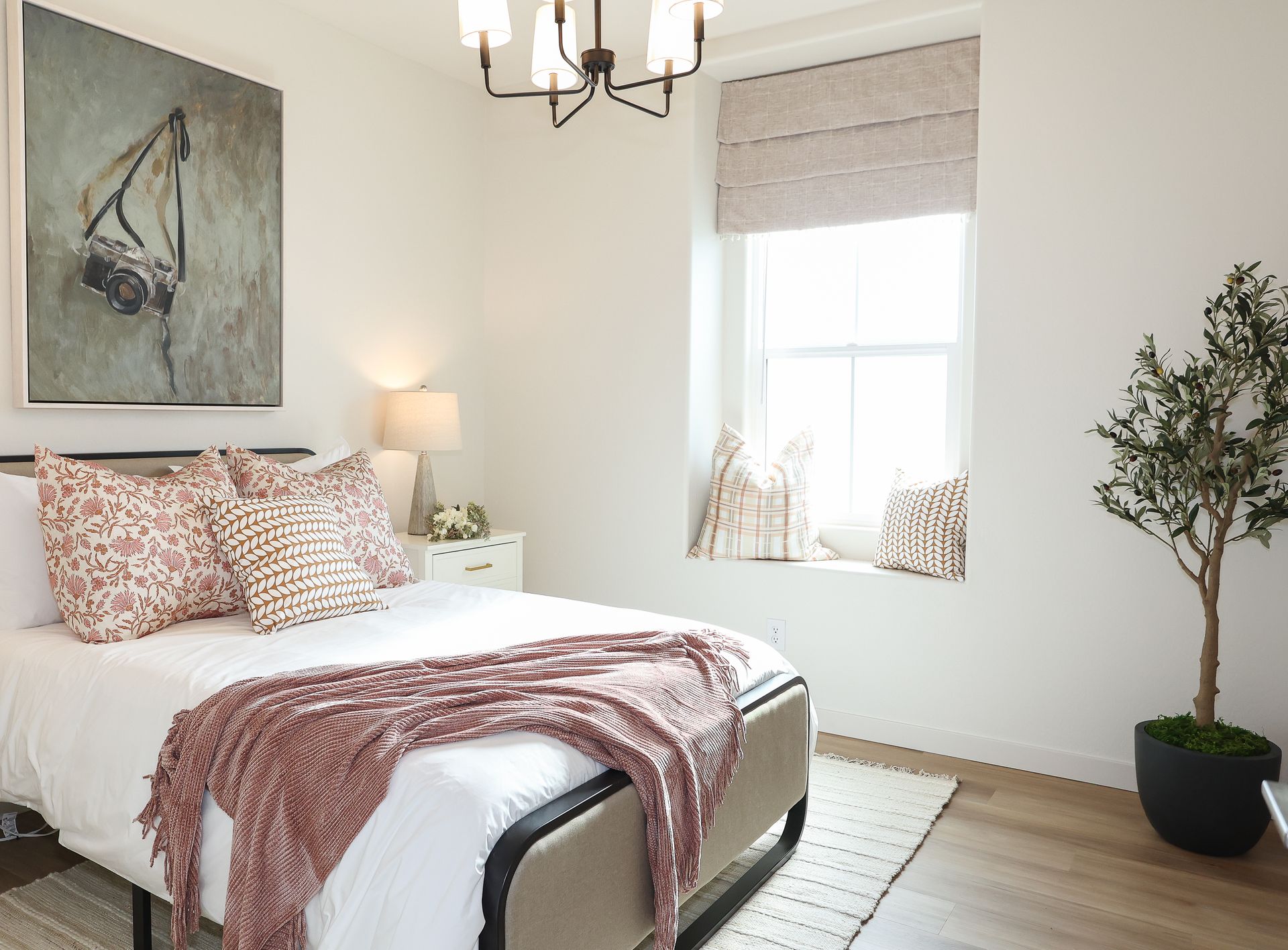 Bright bedroom with white bedding, pink throw, sailboat art, and a potted tree by the window