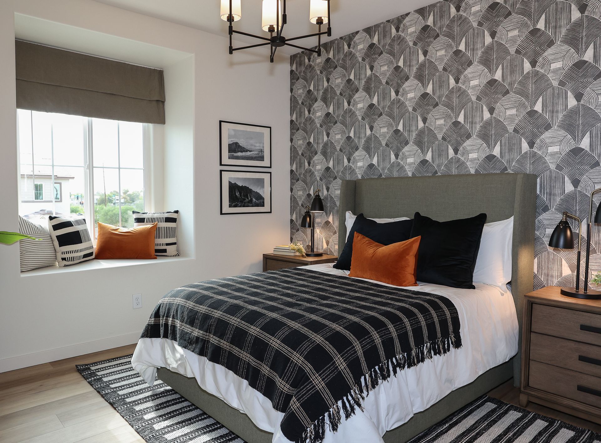 Bedroom with black-and-white patterned wallpaper, gray bed, orange accents, window seat, and chandelier