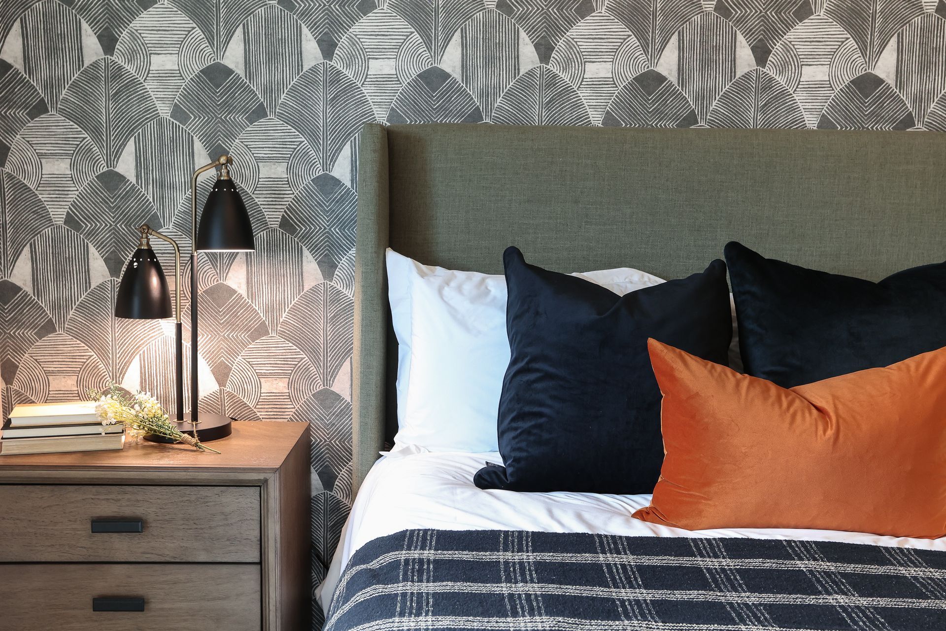 Stylish bedroom with patterned wallpaper, bedside lamp, and bed with navy and orange pillows