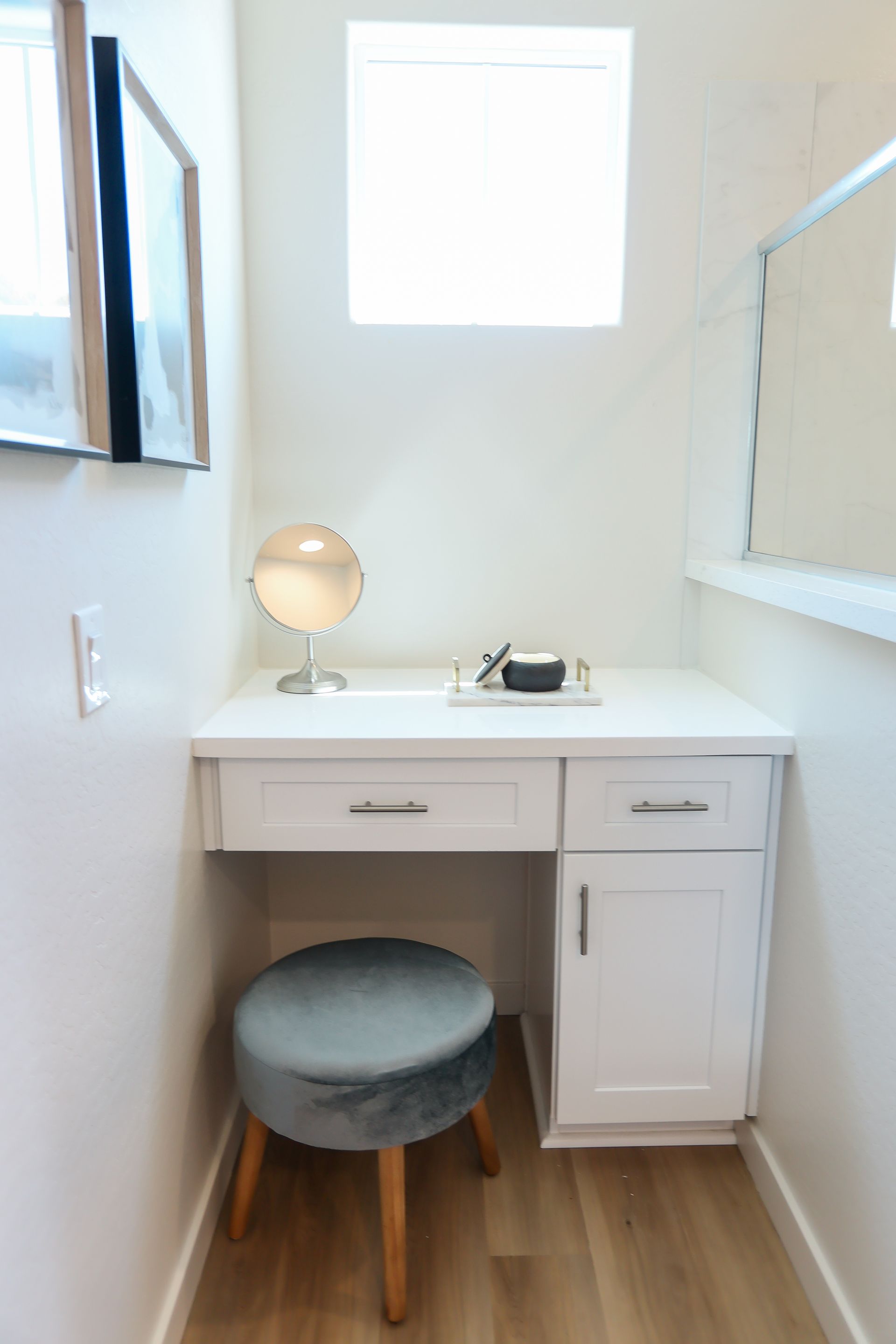 Small white vanity desk with a round stool and lamp in a bright bathroom or dressing area.