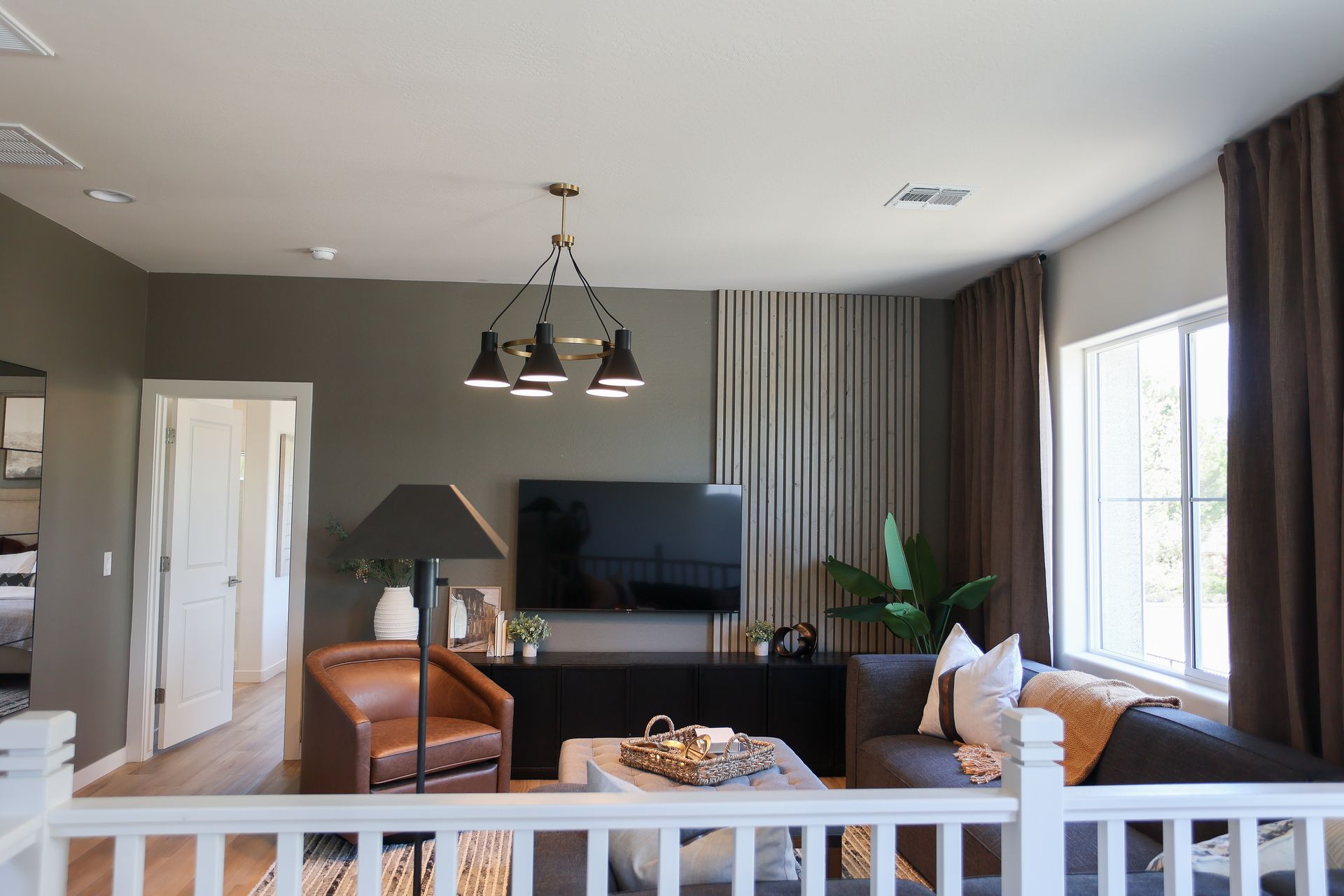 Modern living room with gray walls, leather chairs, TV, pendant lights, and a large window