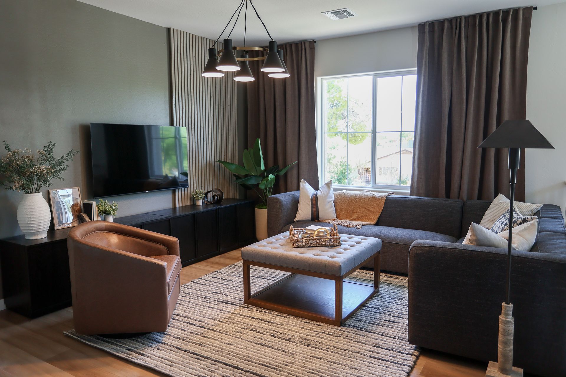 Modern living room with sofa, armchair, coffee table, TV, and large window with curtains