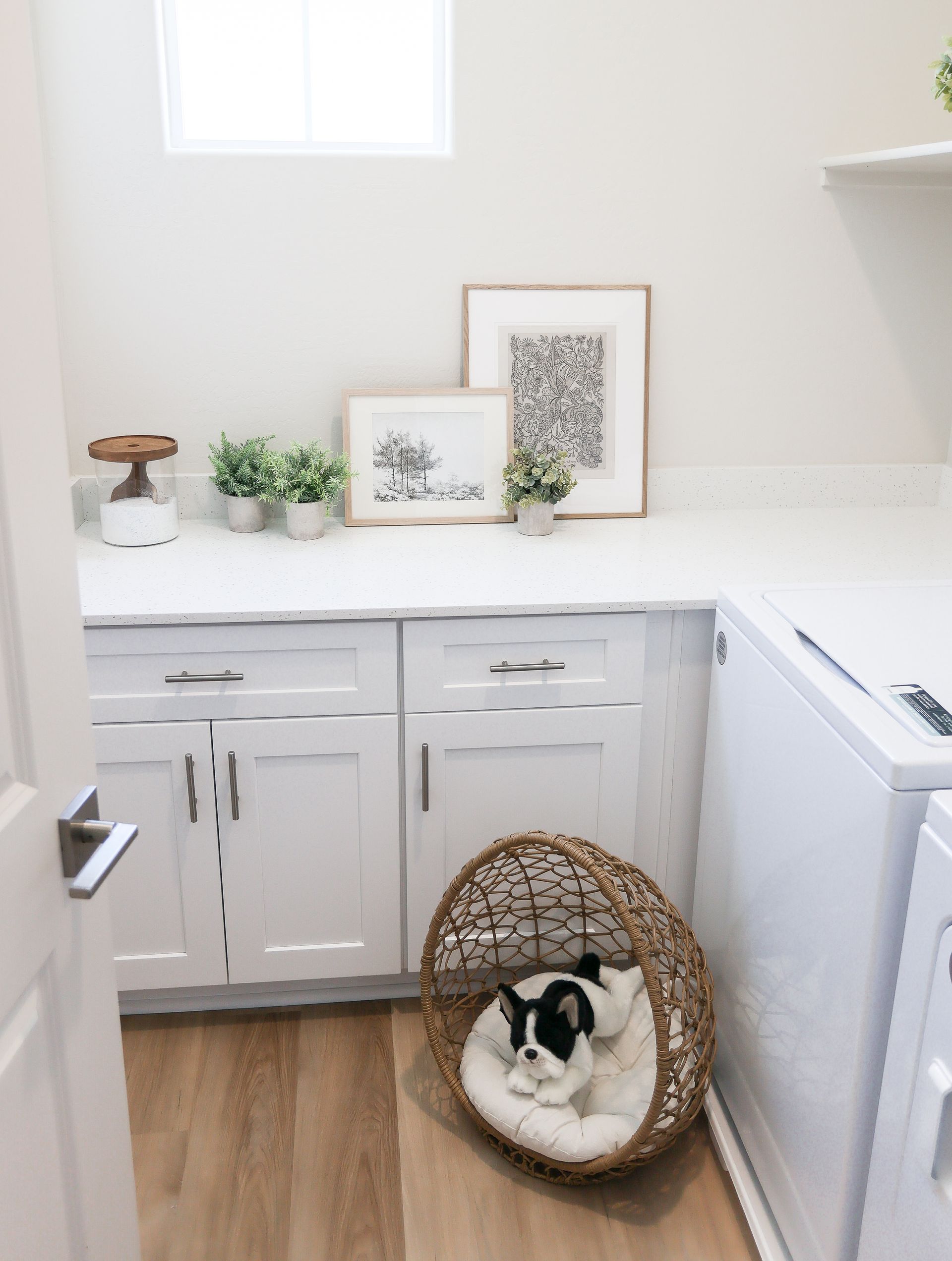 Bright white laundry room with cabinets, countertop decor, and a small dog in a wicker bed on the floor