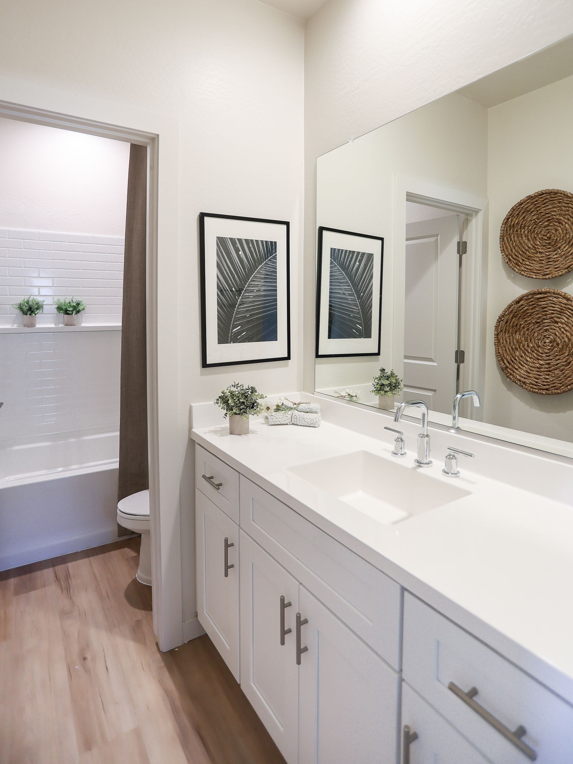 Bright bathroom with white double vanity, large mirror, framed art, and an open doorway to a shower.