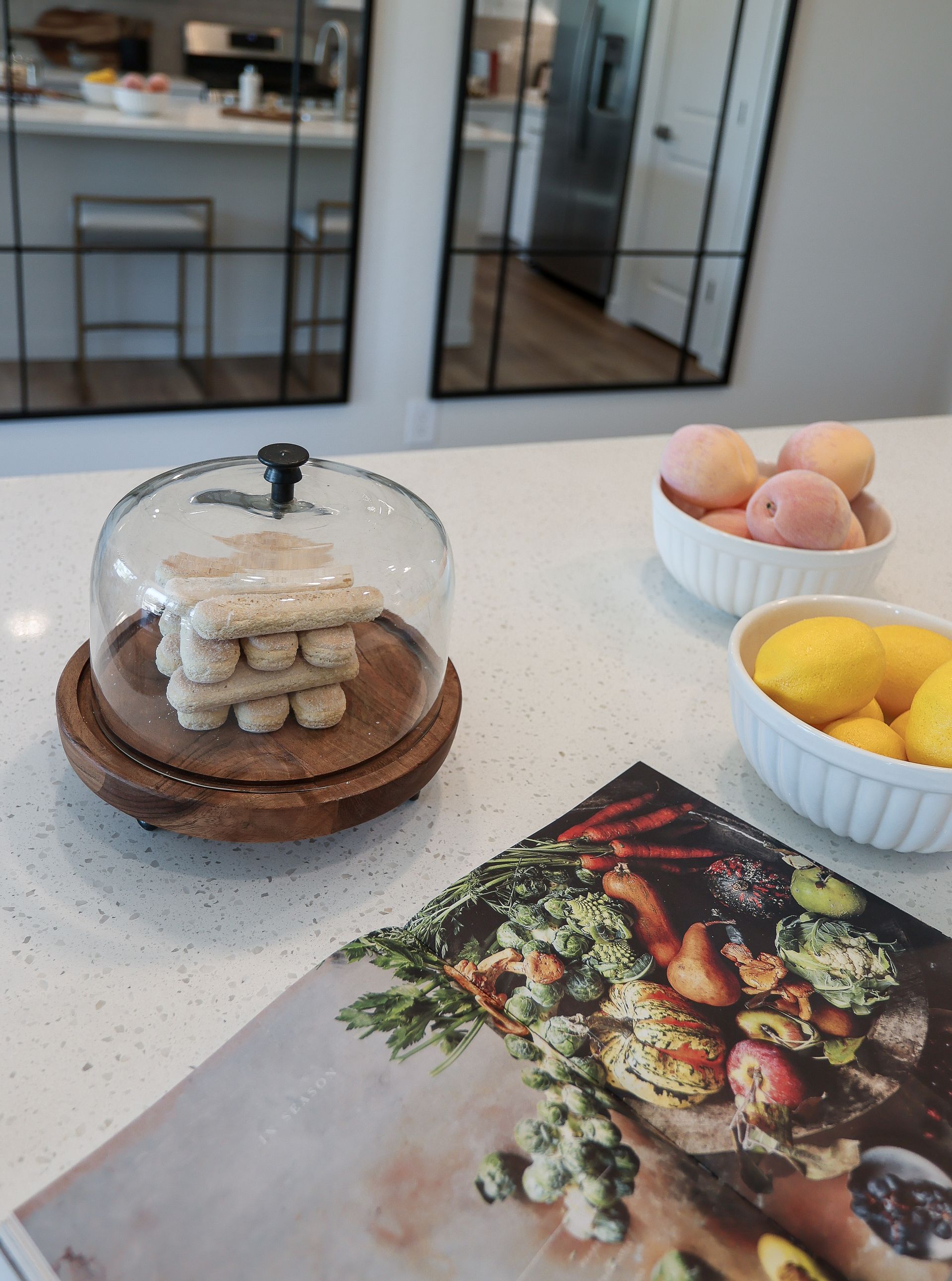 Kitchen counter with glass cookie jar, bowls of fruit, and a cookbook page.