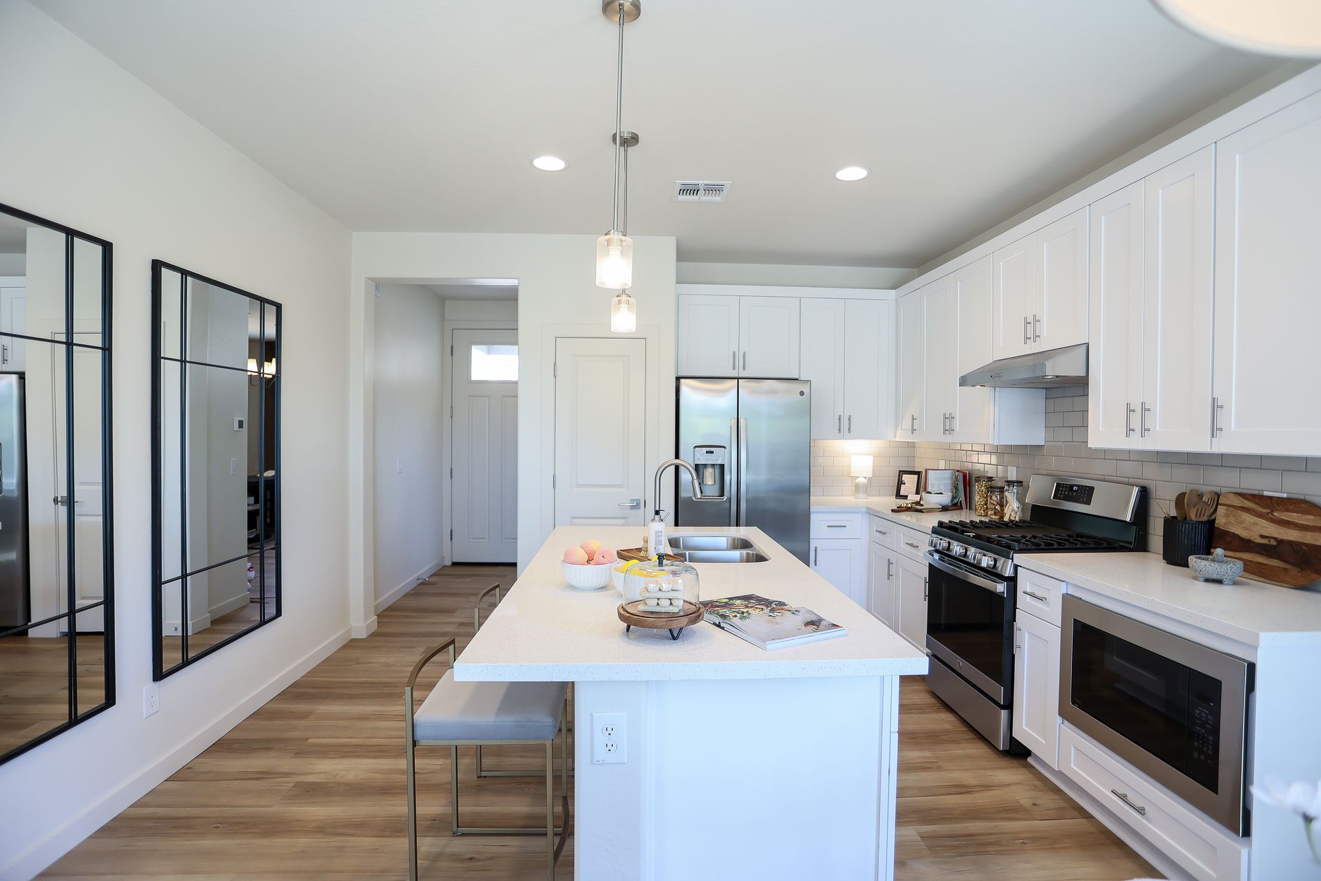Bright modern kitchen with white cabinets, island, stainless appliances, and wood floors