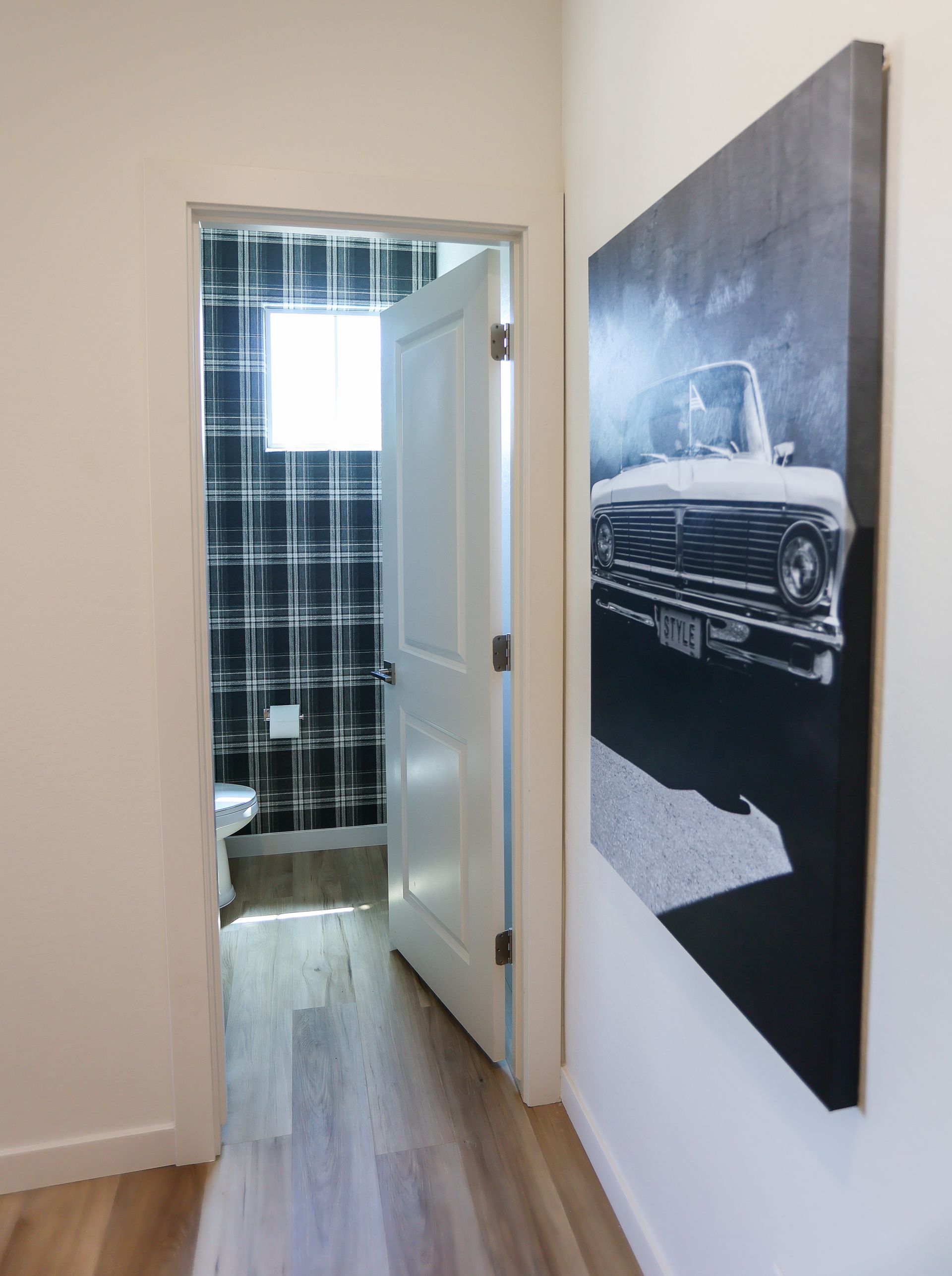 Hallway leading to a bathroom with a blue shower curtain and a car artwork on the wall