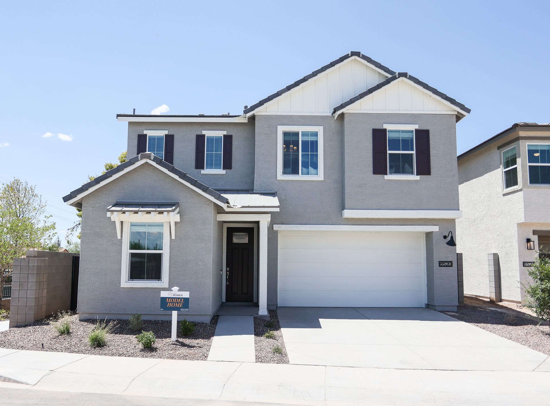 Two-story gray house with white trim, front garage, and a small front porch under a clear sky
