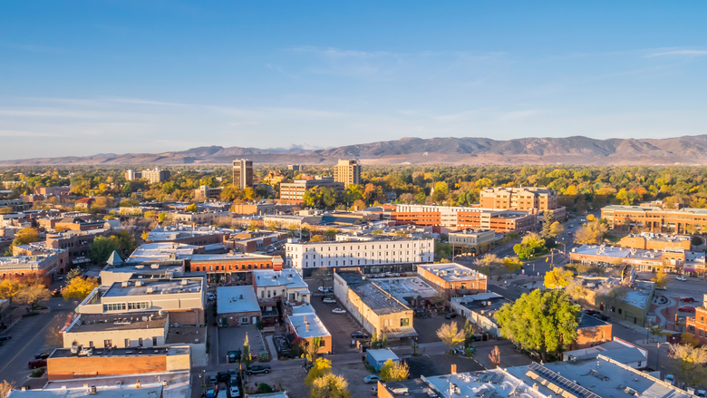 Aerial view of a sunlit town with low buildings, trees, and mountains in the distance.